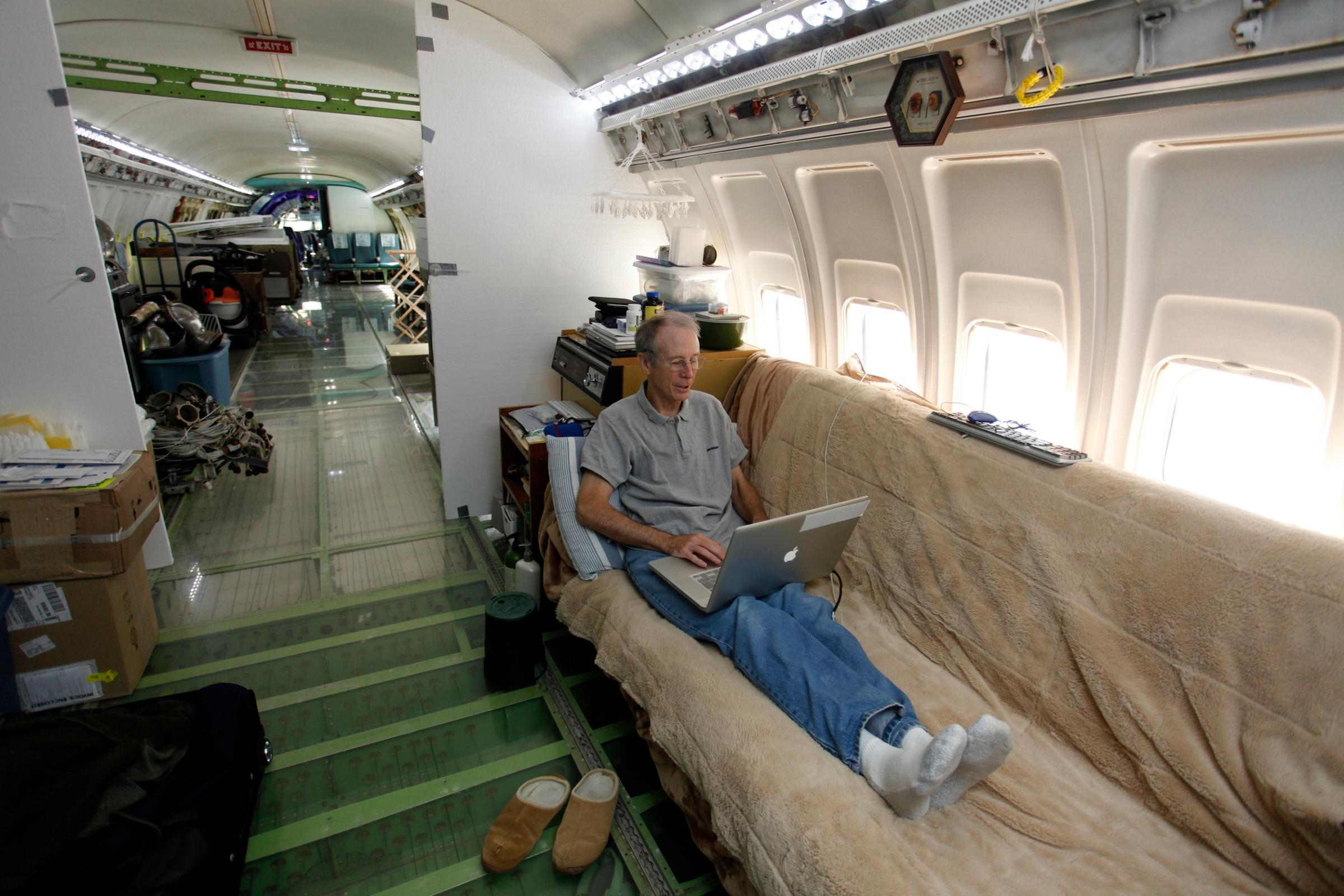 Bruce Campbell sits on his futon bed while using a laptop in his Boeing 727 home in the woods outside the suburbs of Portland, Oregon
