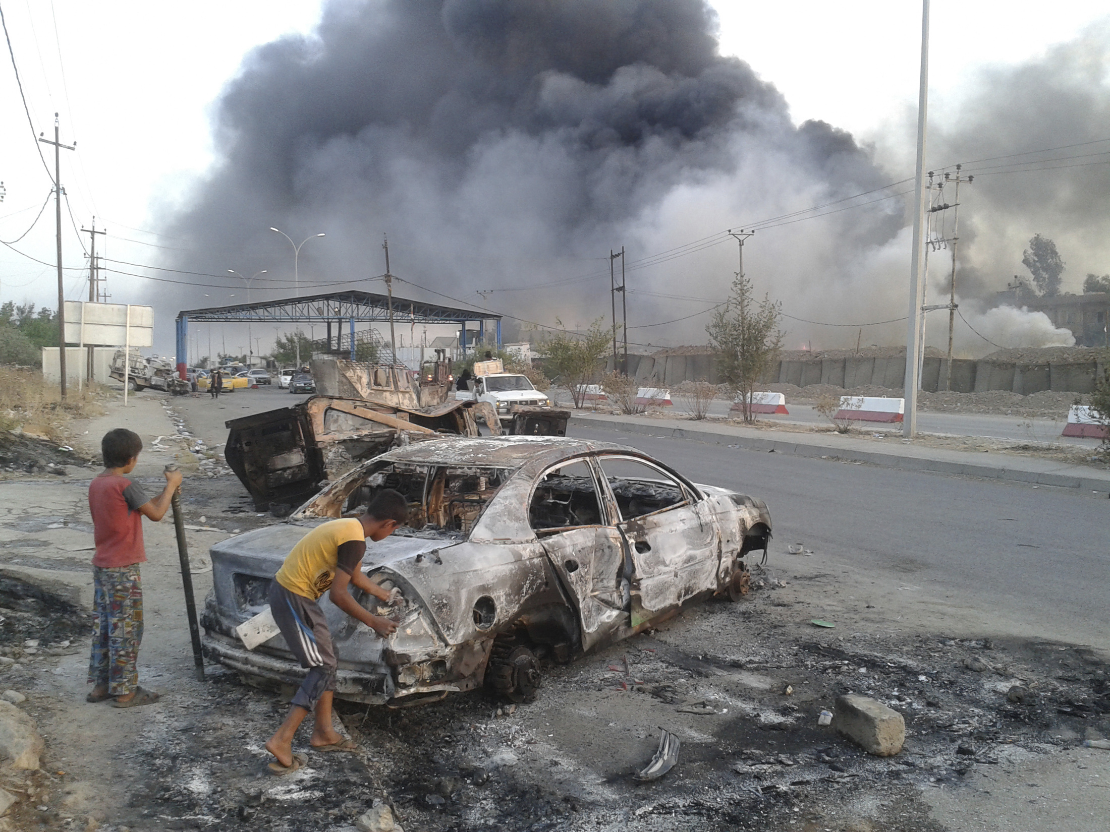 Civilian children stand next to a burnt vehicle during clashes between Iraqi security forces and al Qaeda-linked Islamic State in Iraq and the Levant (ISIL) in the northern Iraq city of Mosul
