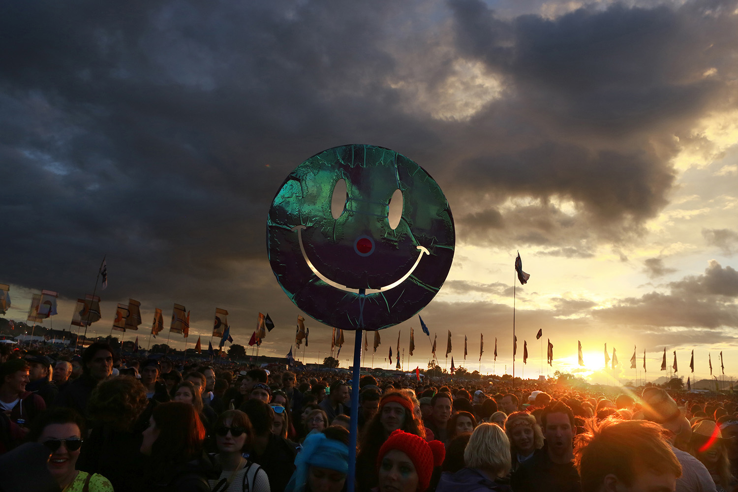 June 27, 2014. A smiley face is held up by a festival-goer as the sun sets in front of the Other Stage at Worthy Farm in Somerset, England, during the Glastonbury Festival