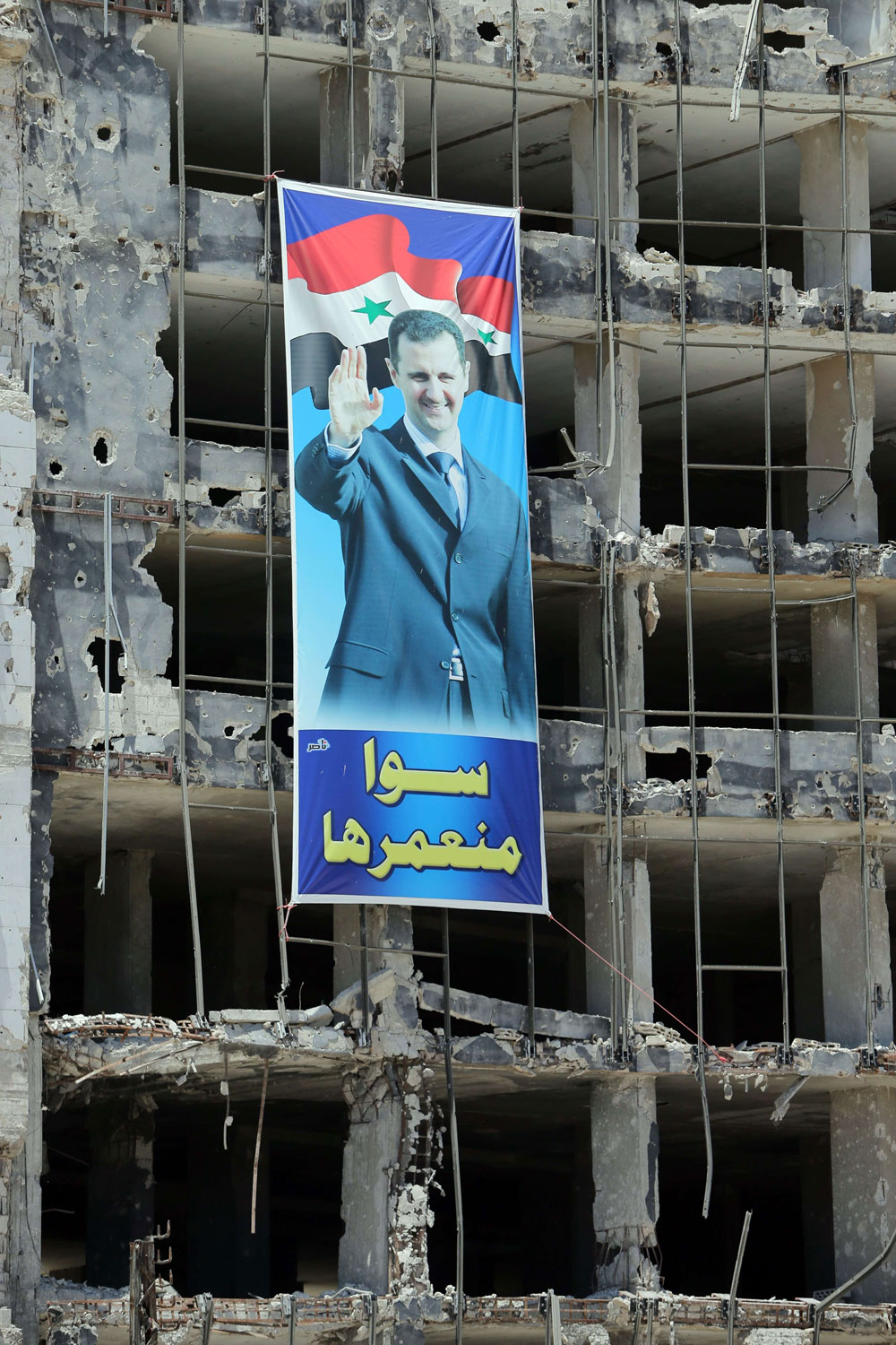 A banner with a picture of Syrian President Bashar Assad with a slogan reading in Arabic,   we build it together   hangs on a destroyed building in the Homs neighborhood of Khaldiyeh on May 3, 2014.