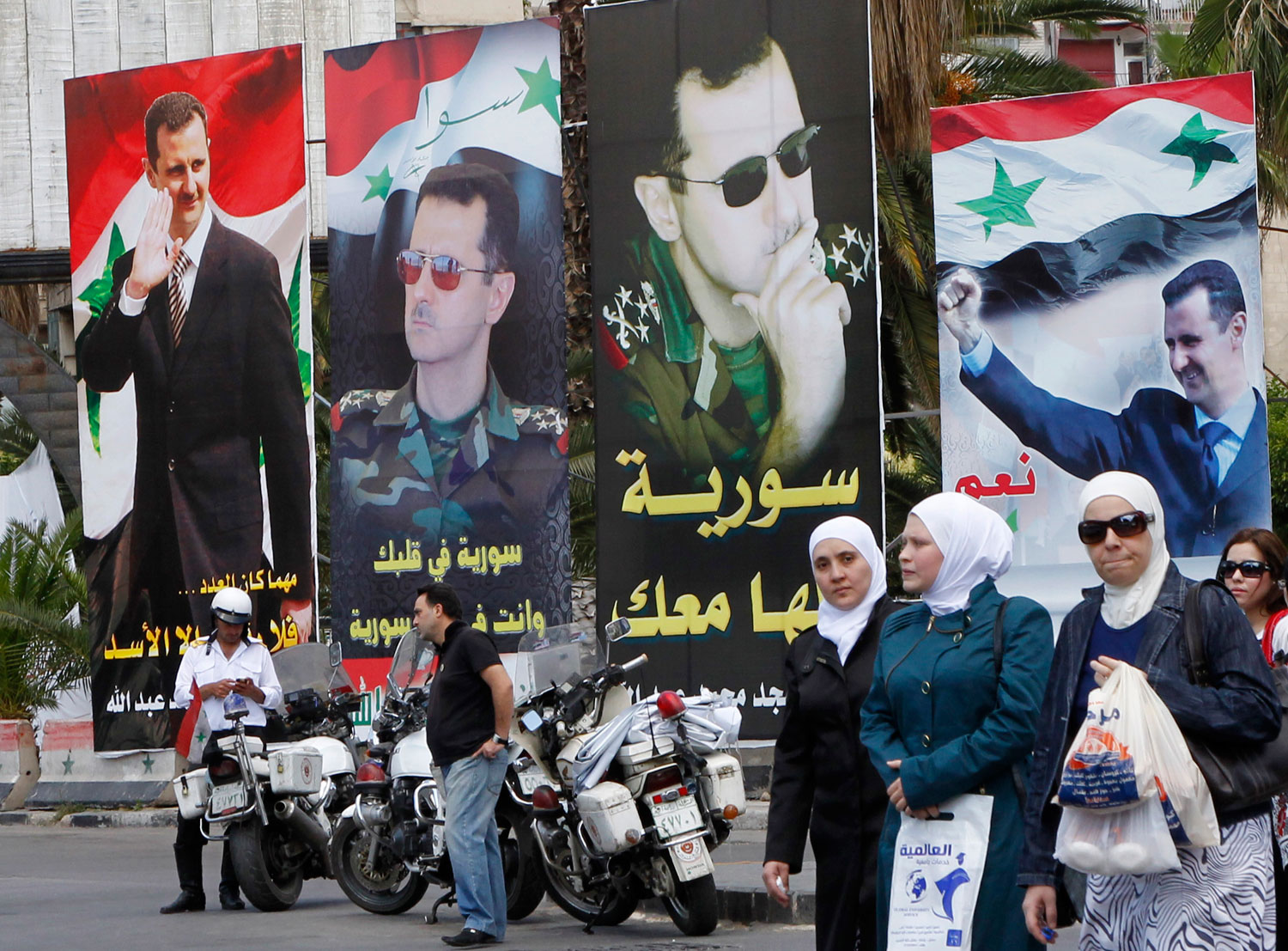 Women walk past election posters of Syria's President Bashar al-Assad along a street in Damascus