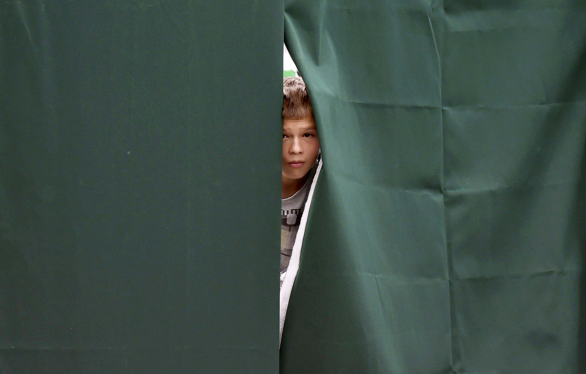 A boy looks through a gap in canvas screening on Court 12 at the Wimbledon Tennis Championships, in London