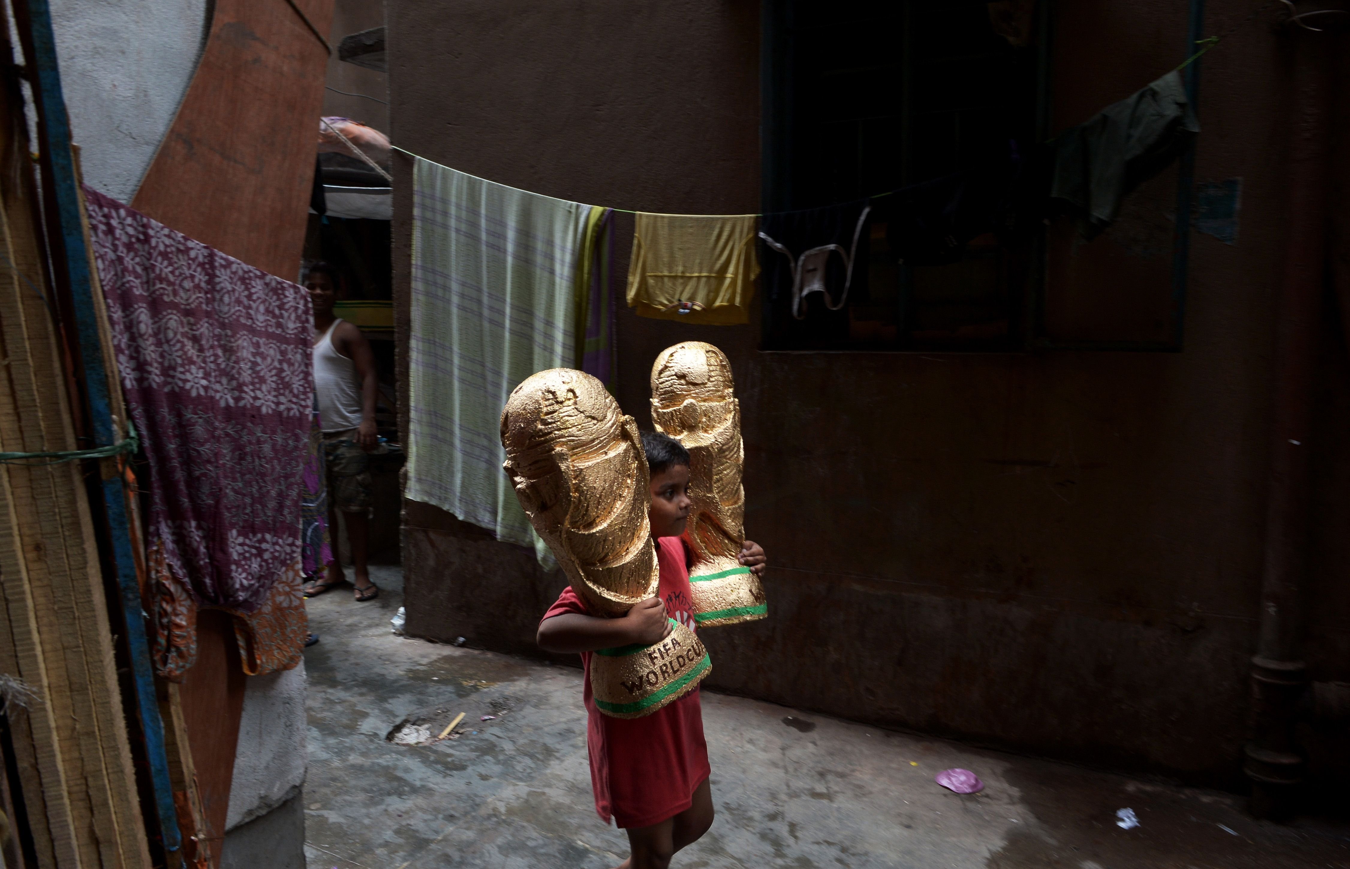 A young Indian boy carries a pair of models of the 2014 FIFA World Cup trophy made by artisans to a godown - warehouse in Kolkata, India on June 18, 2014.