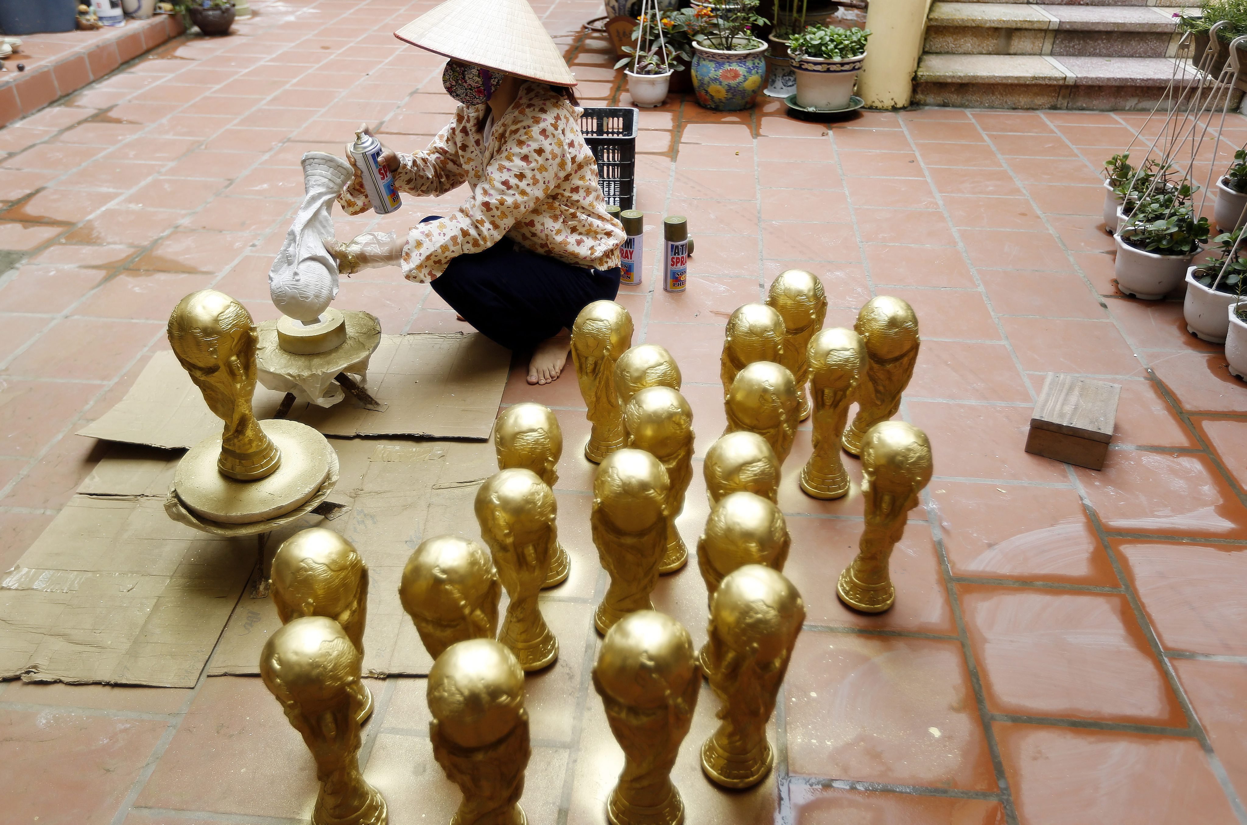 A woman paints a gypsum-made FIFA World Cup trophy at her home, in Bat Trang pottery village, Hanoi, Vietnam on June 19, 2014.