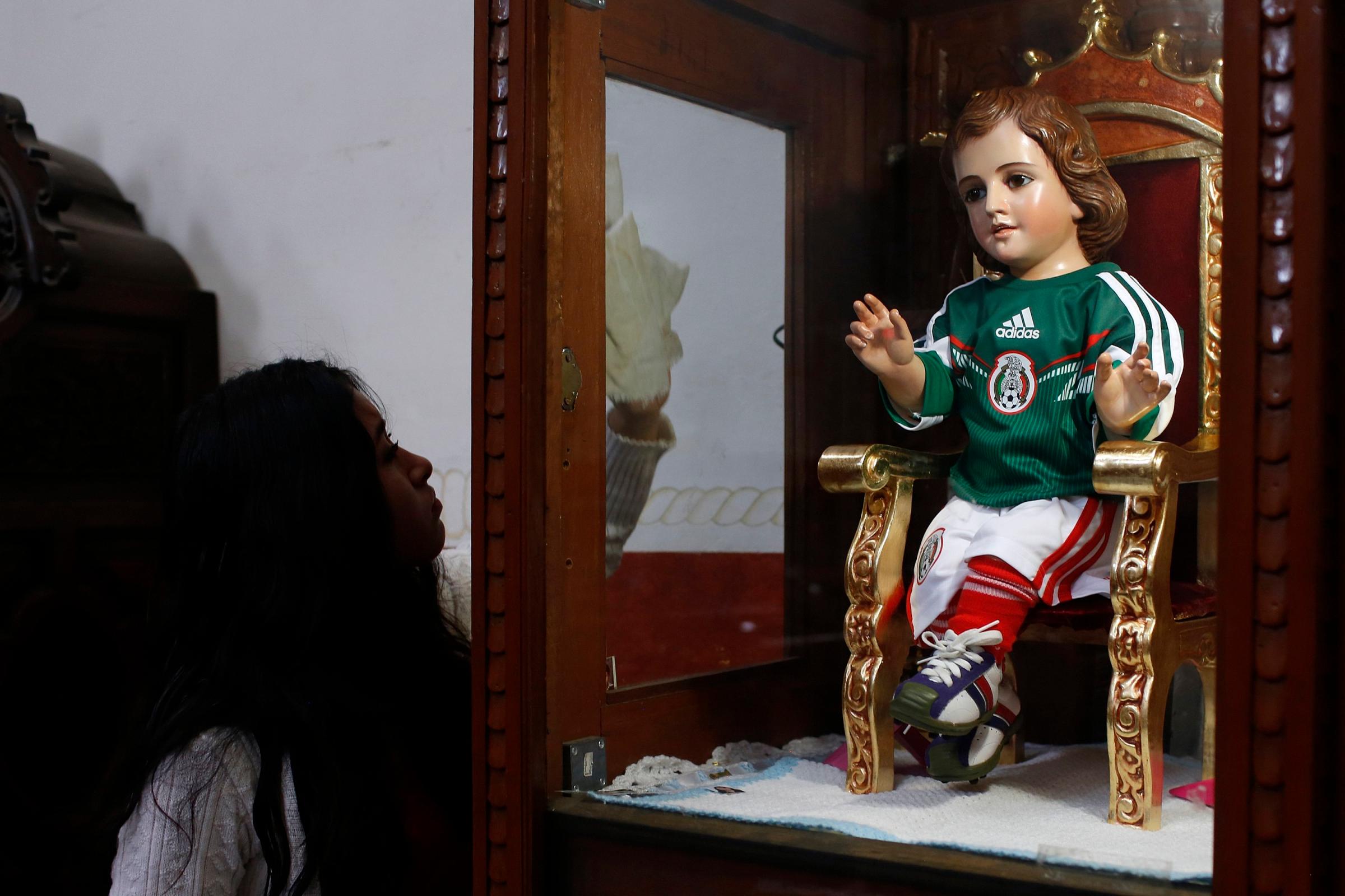 A woman cleans a glass cabinet with a baby Jesus statue dressed in a version of the national soccer team jersey at a church in Mexico City on June 12, 2014.