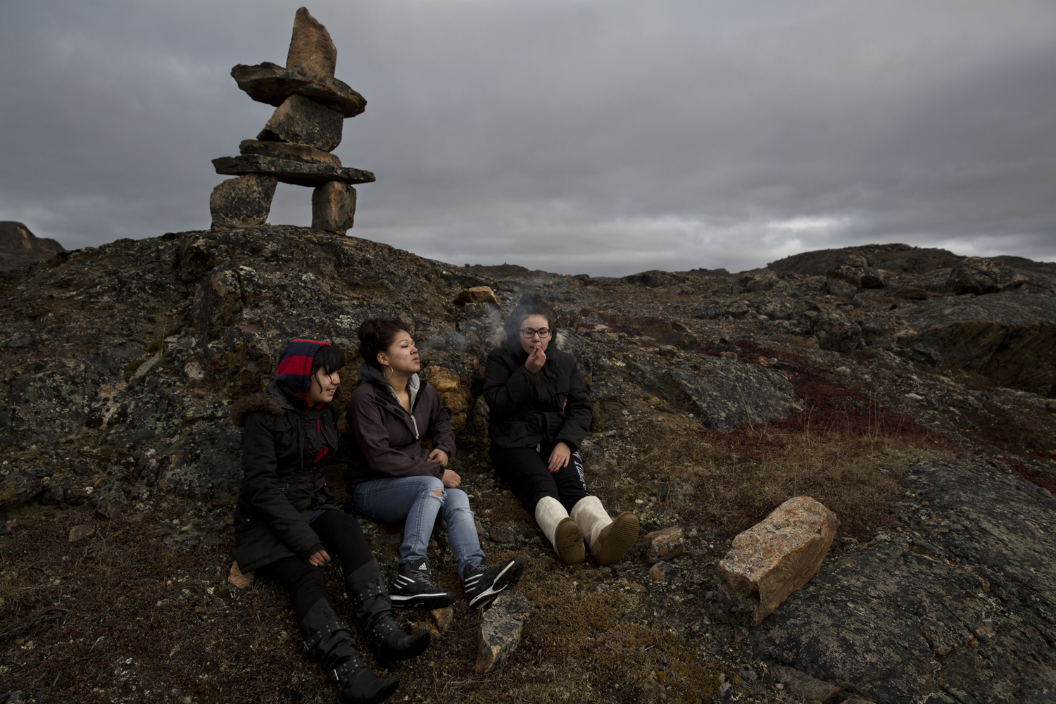 Iqaluit, Canada, Oct. 5, 2013. Kelly Amaujaq Fraser (left) smokes with her friends Vernuh Kanatsiak (middle) and Beth Idlout-Kheraj (right) under an inuksuk stone landmark. The inuksuk is traditionally used by the Inuit as a marker for navigation and is often thought of as a symbol of Inuit culture in Canada.