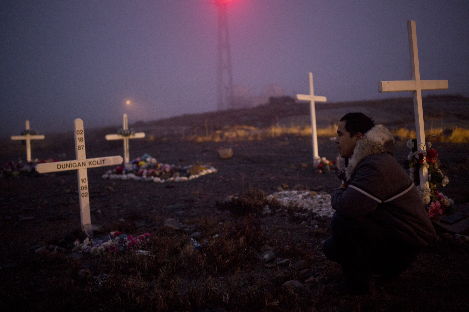 RANKIN INLET, CANADA - OCTOBER 12 Brian Tagalik, 28, visits the grave of his friend Dunigan Kolit, who killed himself when he was 15-years-old, in Rankin Inlet, Canada on Oct. 12, 2013. The two played hockey together as teenagers. Brian says that he “truly believes Dunigan is one of those guys who doesn’t know he’s dead yet, because he was so full of life.” According to Brian, Dunigan’s grandparents raised him because his mother was an alcoholic. As Brian walks throughout the cemetery, he points out the graves of almost a dozen of his friends who died of suicide. According to Health Canada, the incidences of suicide in Inuit youth are among the highest in the world, 11 times the national average. Brian grew up with many of his friends taking their lives. He says, “if I get a phone call at any point in the morning before eleven, I know it’s someone telling me another friend has died. I got rid of my phone, because I just don’t want to know anymore.” At points in time, Brian has considered taking his own life. Since then, Brian has become an activist, trying to break the silence and speak out about taboo topics that Inuit youth face. He tries to share his own story, and counsel people at risk of suicide. Earlier this year, he recorded a song called “The Struggle” with fellow musician Kelly Fraser, which speaks to their shared experience with suicide and the harsh social realities of living in the arctic. The song, released on local radio stations and online, resonates with many Inuit youth. (Ed Ou/Reportage by Getty Images)https://soundcloud.com/user248977338/the-struggle-feat-kelly-fraser