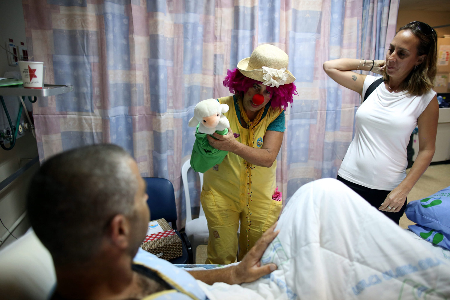 An Israeli woman dressed as a clown tries to cheer up an injured Israeli soldier who was wounded in fighting in the Gaza Strip, in the Soroka Hospital in Beersheba, Israel, July 30, 2014.