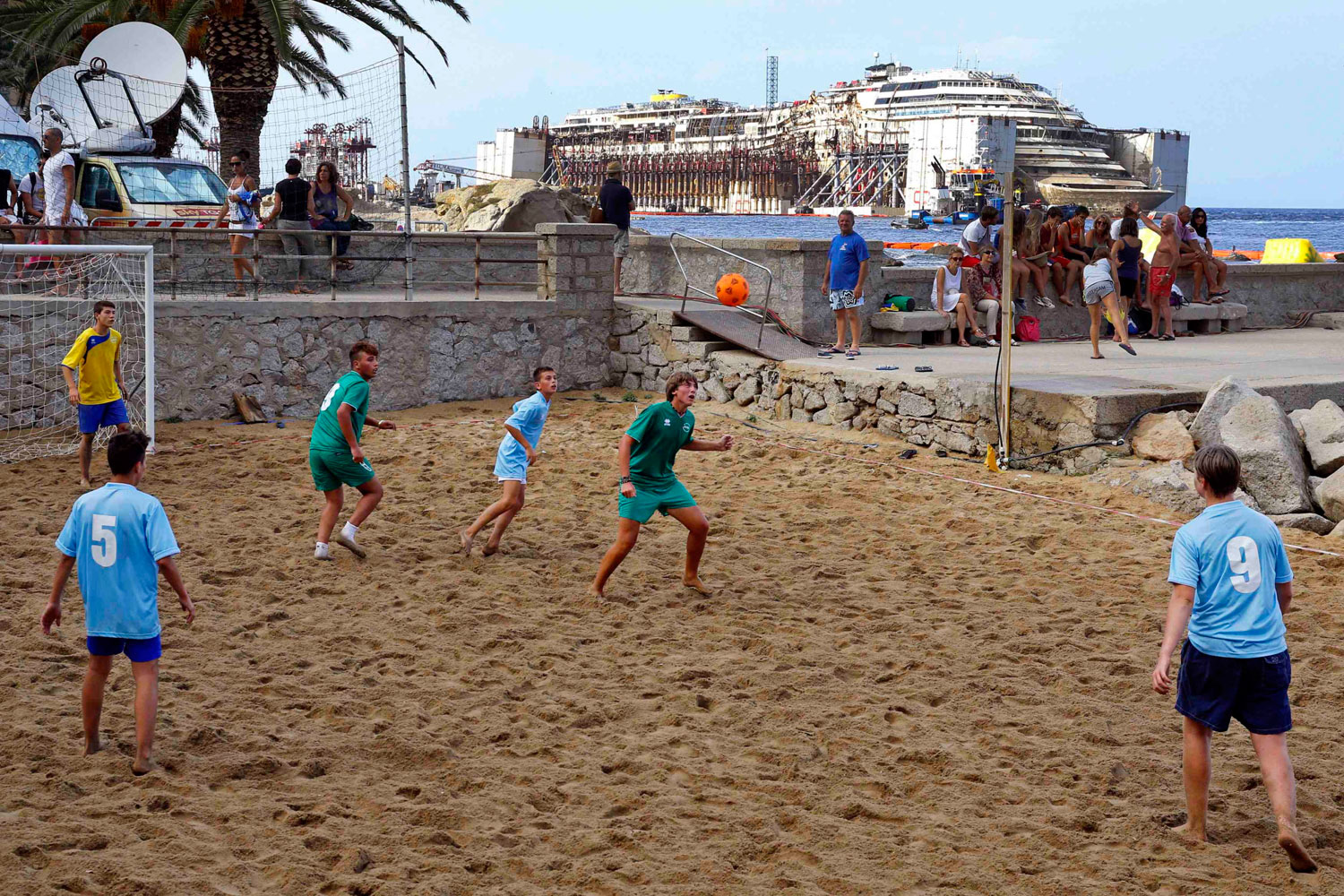 Youths play football at a beach as the Costa Concordia cruise liner is seen during its refloating operation at Giglio harbour