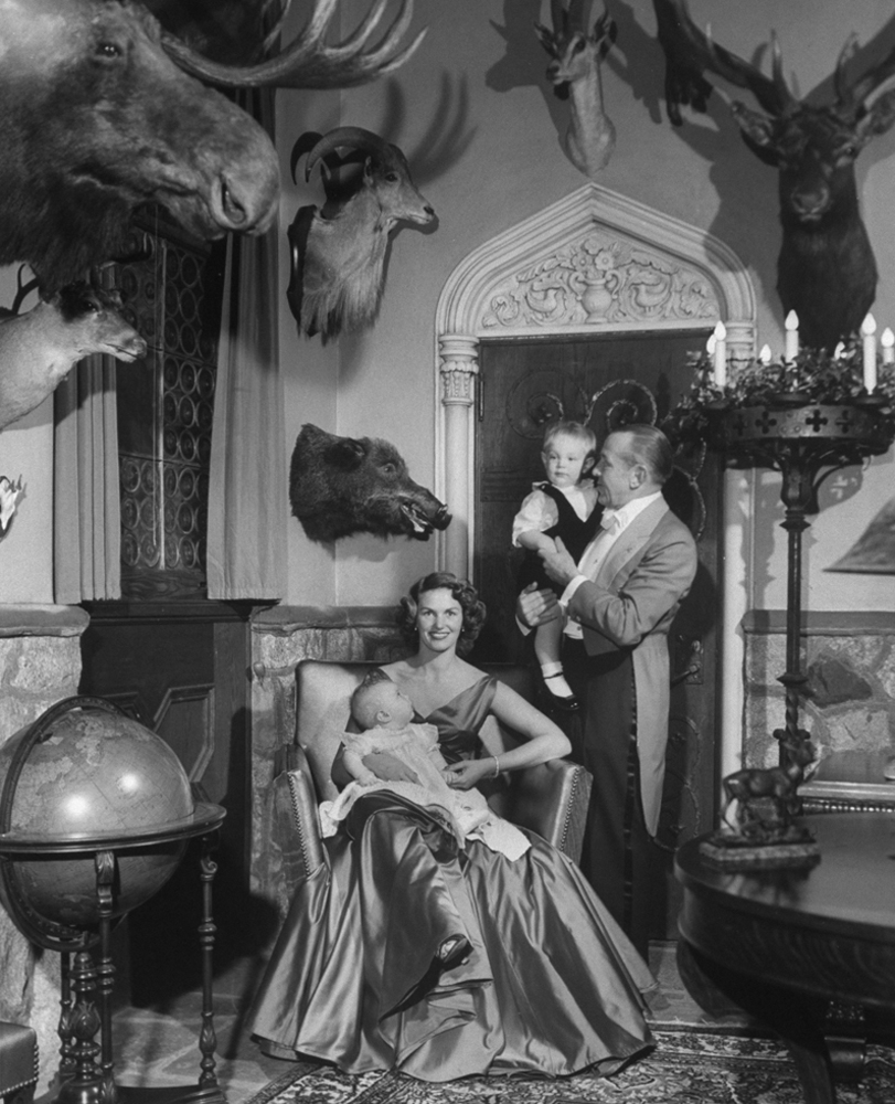 In the trophy-filled gun room of their mansion, August A. Busch Jr. and his wife Trudy, 28, hold baby Beatrice Alice and Adolphus Busch IV.