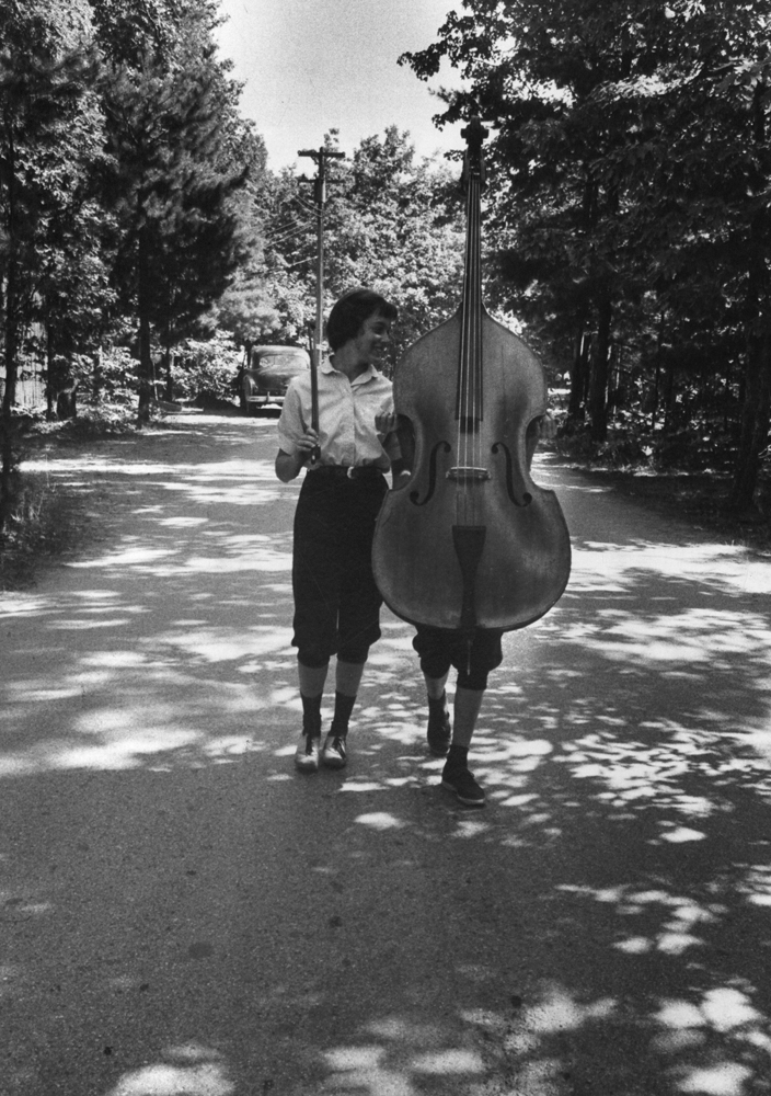 Staggering under her towering armful the young lady with her companion--both students at Interlochen, Mich. National Music Camp--is giving an outsized demonstration of the way Americans put their idle summer hours to profitable use.