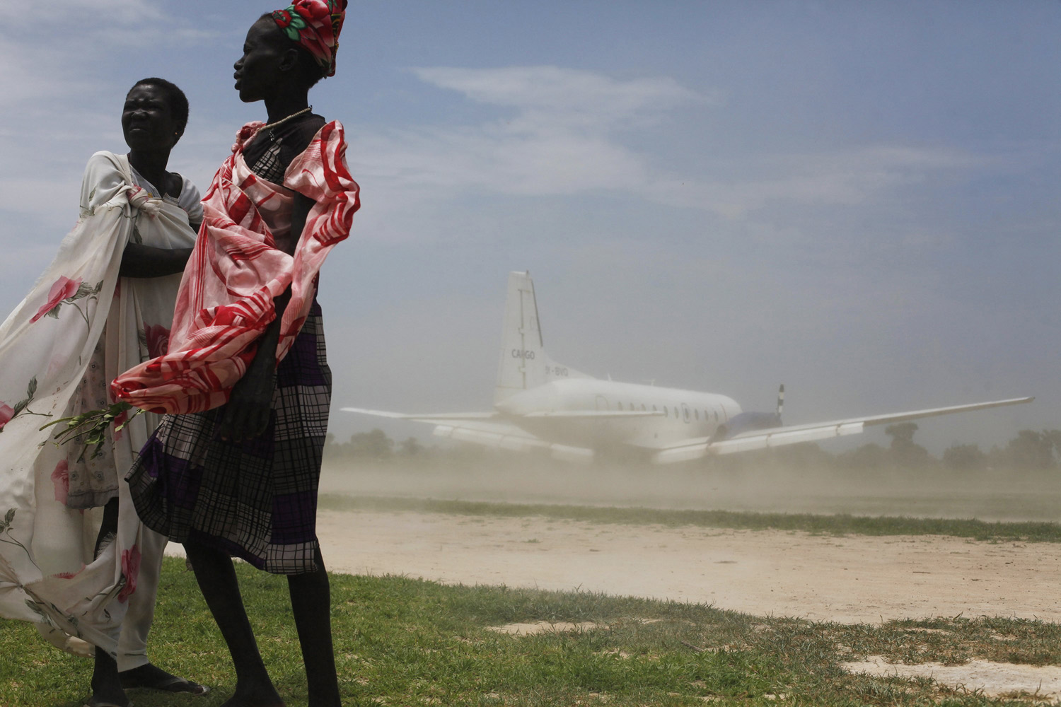 Women try to avoid dust as a plane, carrying nutrition supplements brought in by Medecins Sans Frontieres, lands in Leer