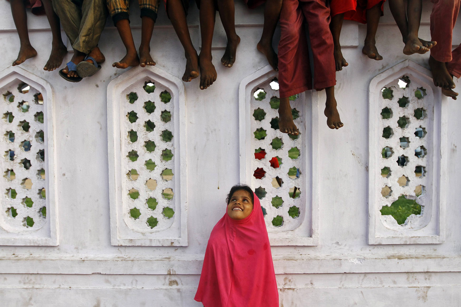 A Muslim girl looks up while some boys sit on a wall, inside the premises of a mosque, as they wait for Iftar (breaking fast) meal during the holy month of Ramadan in the southern Indian city of Chennai