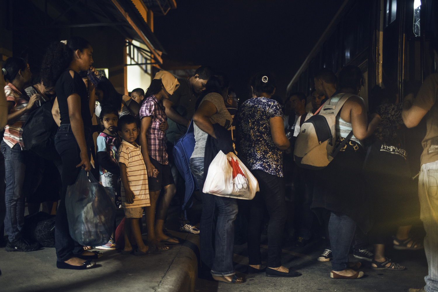A crowd of departing migrants bound for the United States boards a bus that will take them overnight to the Honduras-Guatemala border and from there North to Mexico. San Pedro Sula, Honduras. July 15th, 2014.