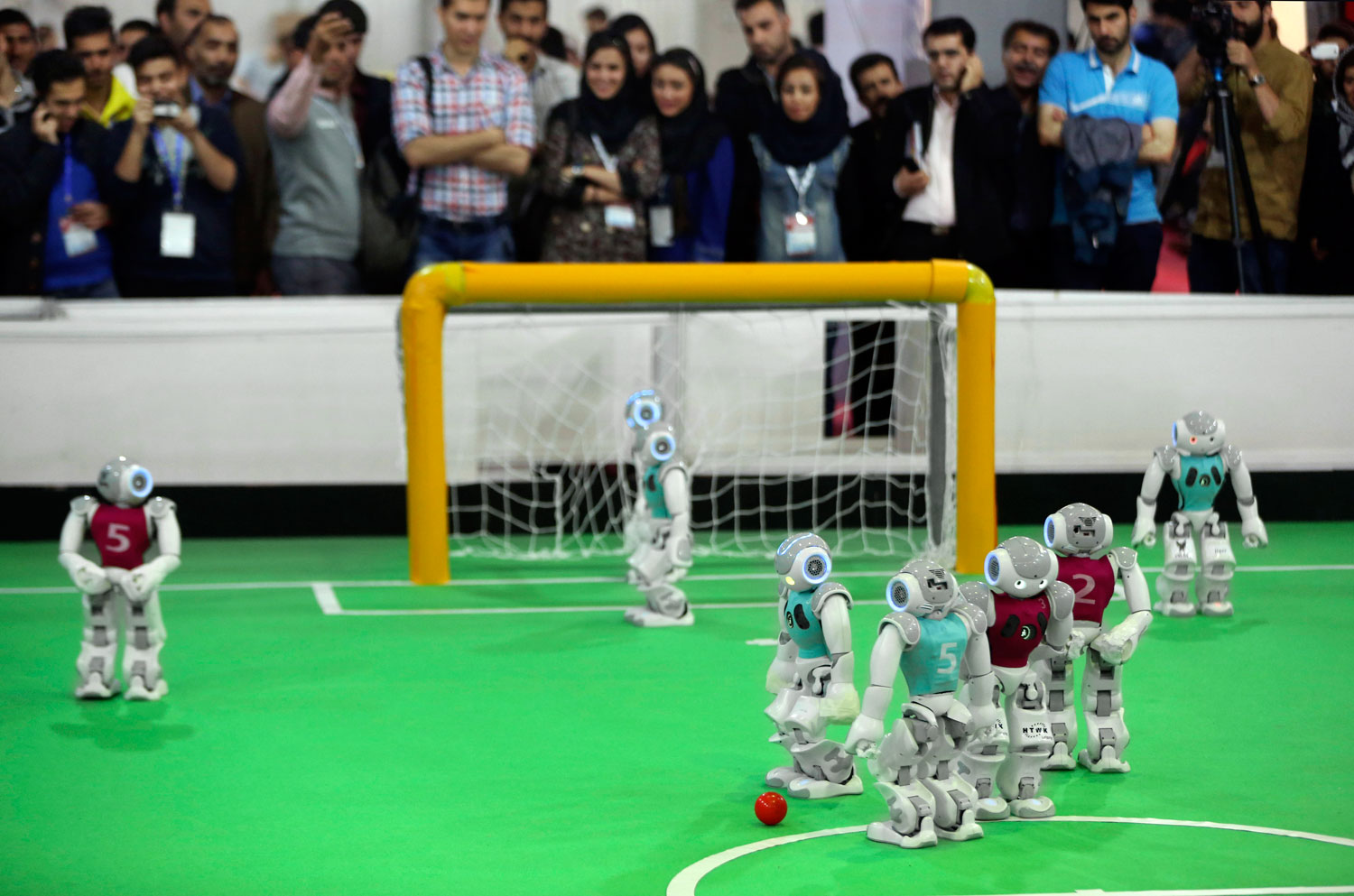 Humanoid robots play during a soccer match while visitors follow the competition in the international robotics competition, RoboCup Iran Open 2014, in Tehran, Iran on April 10, 2014.