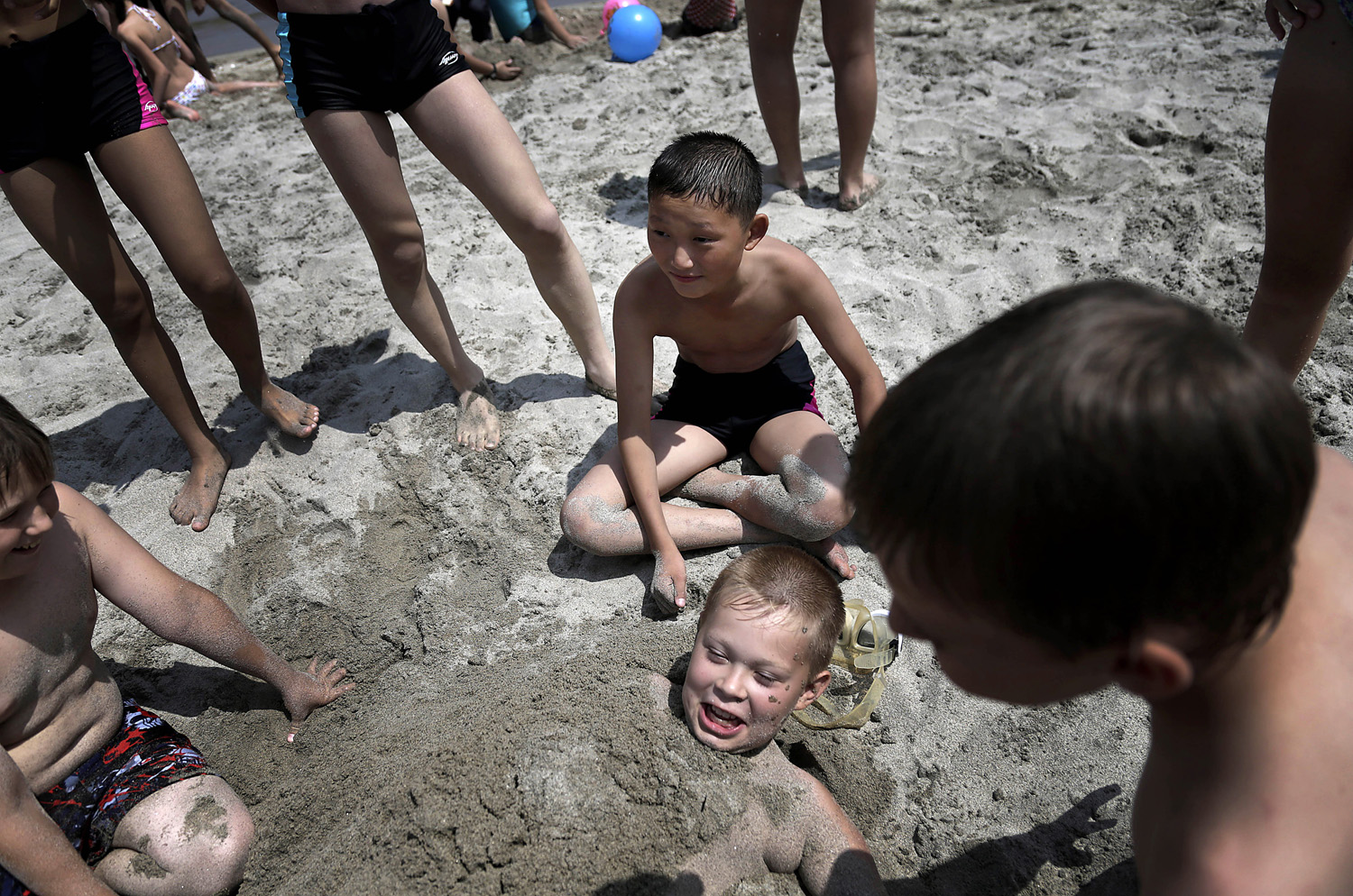 Kim Sun Gun, 12, of North Korea, center, smiles as he watches other students bury Russian student Konstantin Kostya, 10, in the sand at the Songdowon International Children's Camp, Tuesday, July 29, 2014, in Wonsan, North Korea.