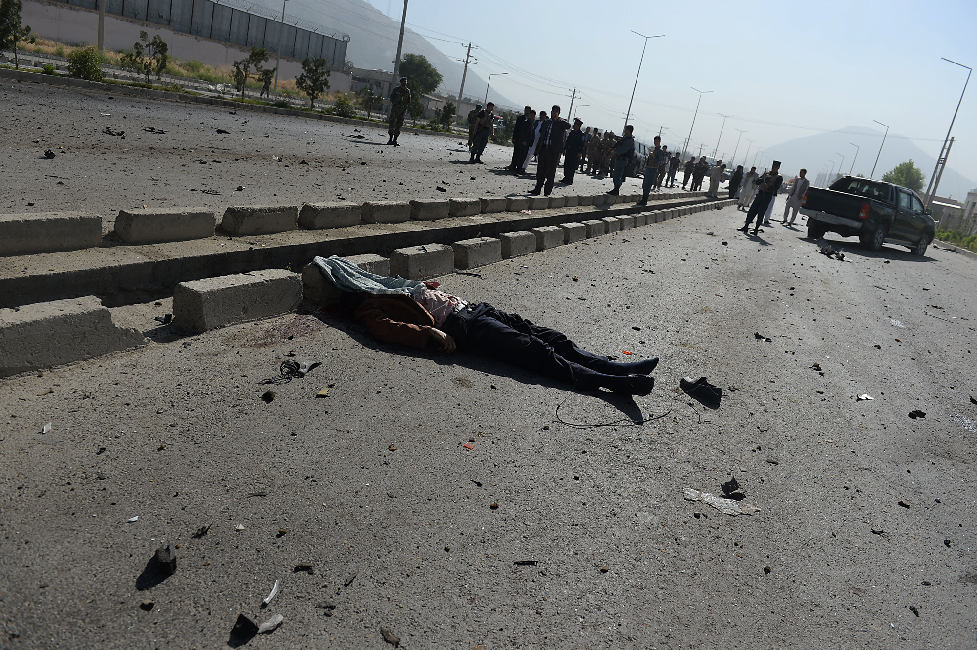 A victim's body lies on the road as Afghan security forces inspect the site of a suicide attack in Kabul on June 21, 2014.