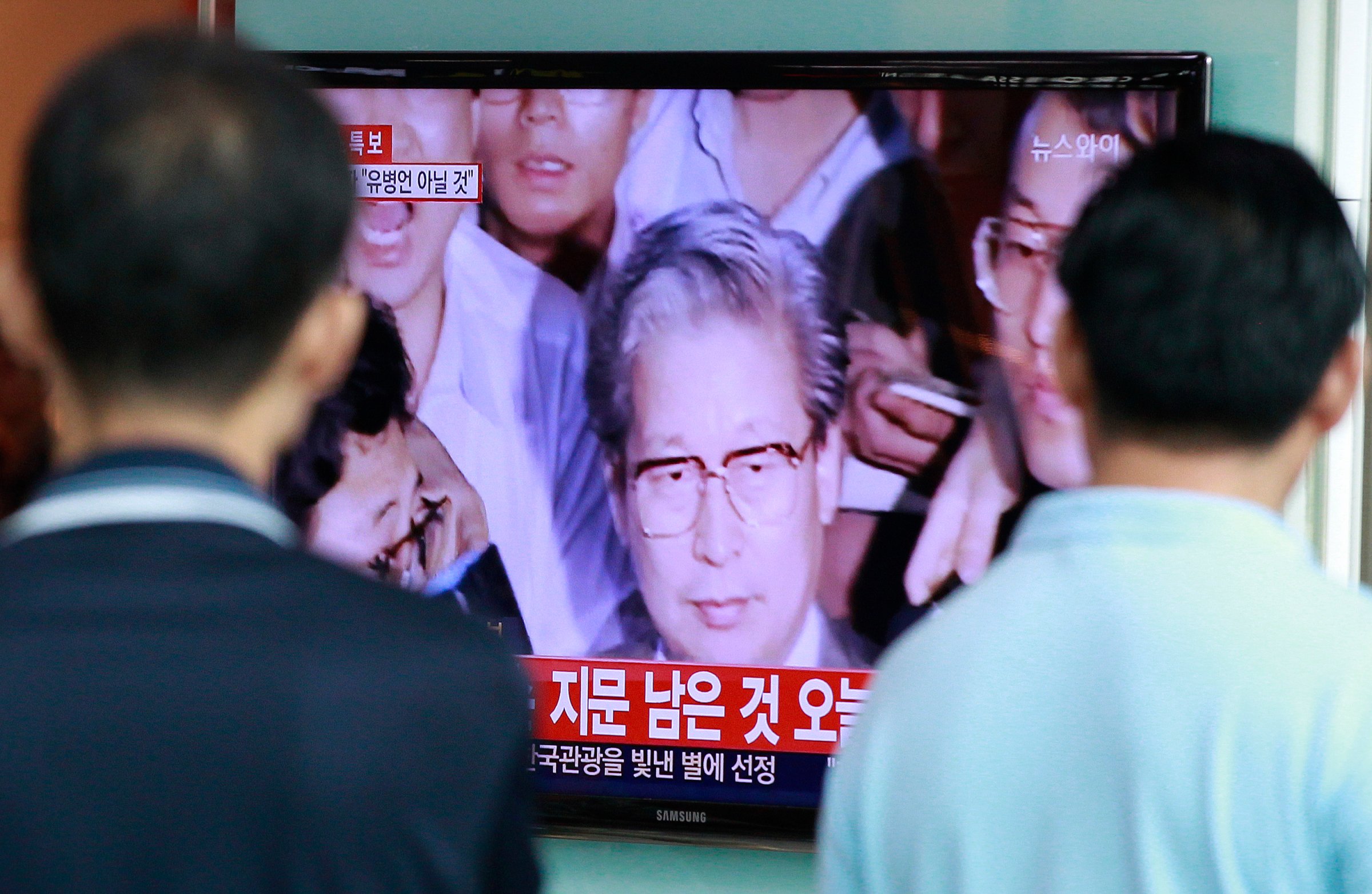Passersby watch TV news showing Yoo Byung-eun, the fugitive owner of the sunken ferry Sewol, at Seoul Railway Station in Seoul on July 22, 2014.