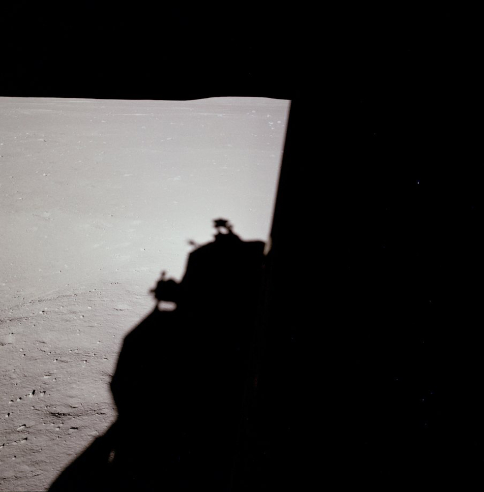 Down-Sun (west) view of lunar surface just after landing with the LM shadow, lunar horizon and a partial view of a shallow crater to the left of the LM shadow.