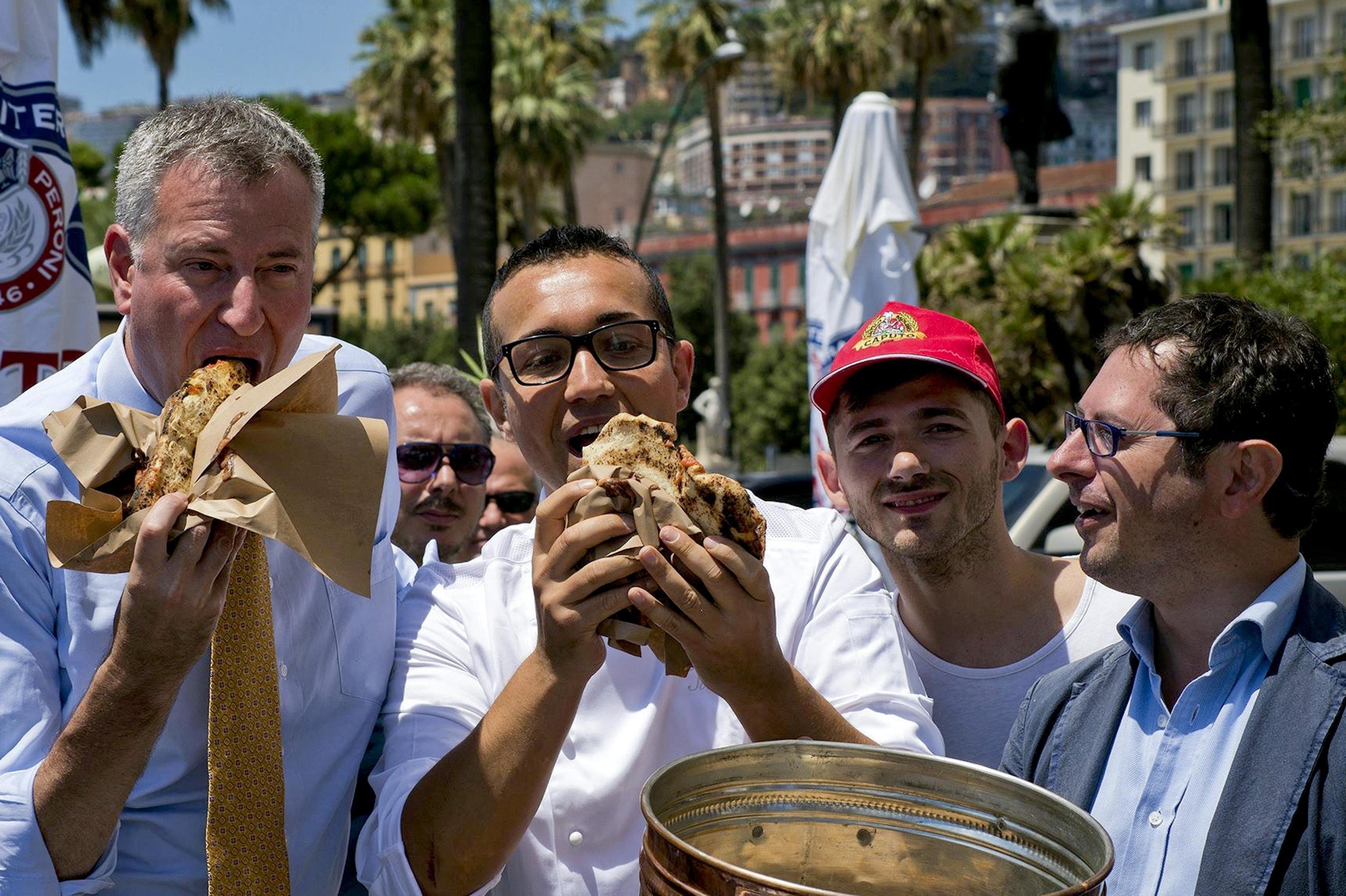 New York mayor Bill de Blasio (L) eats a pizza made by Napoli's pizza chef Gino Sorbillo (2nd from L) in Naples, Italy on July 23, 2014..