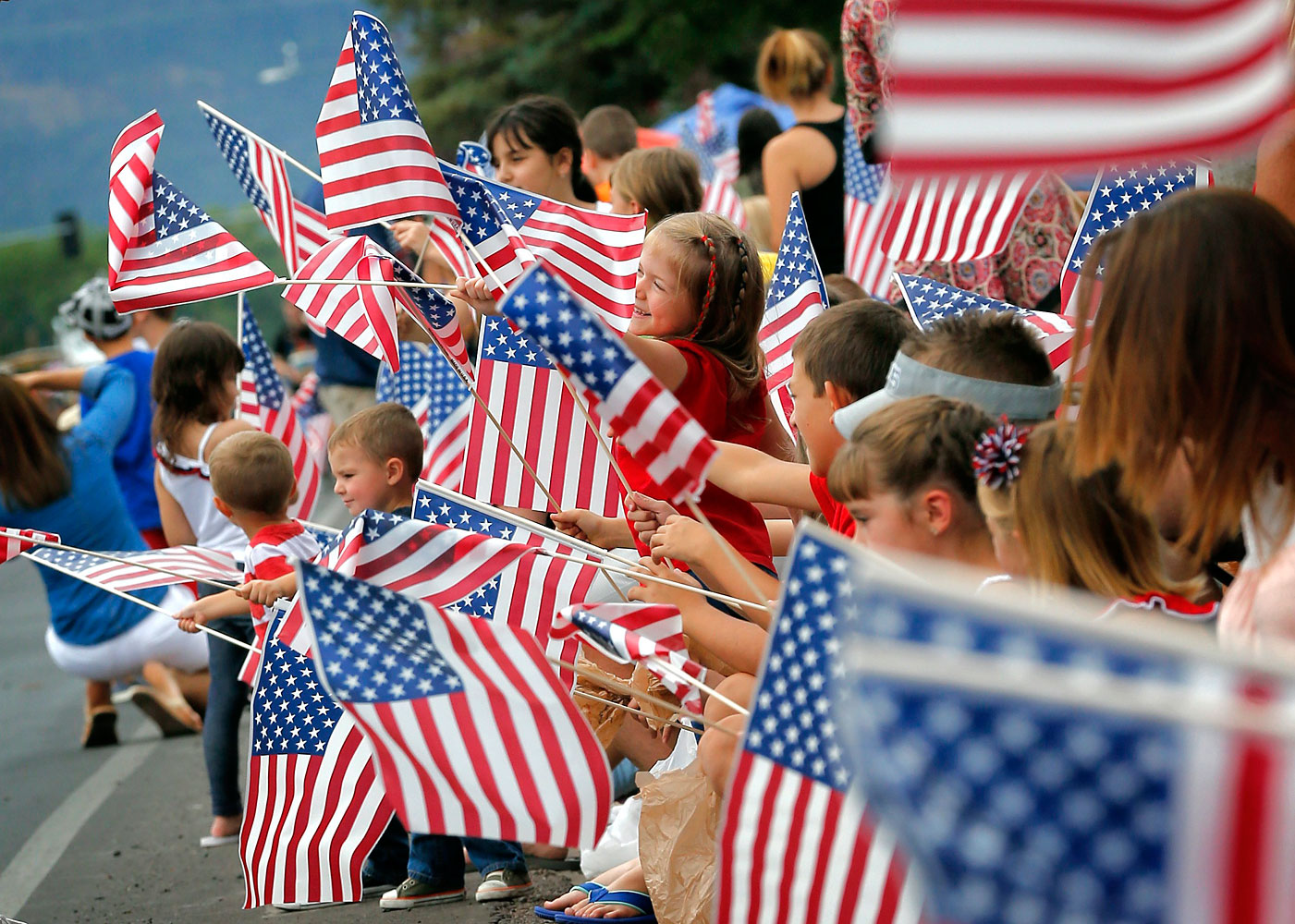 People wave flags as the Independence Day parade rolls down Main Street, July 4, 2014, in Eagar, Ariz.