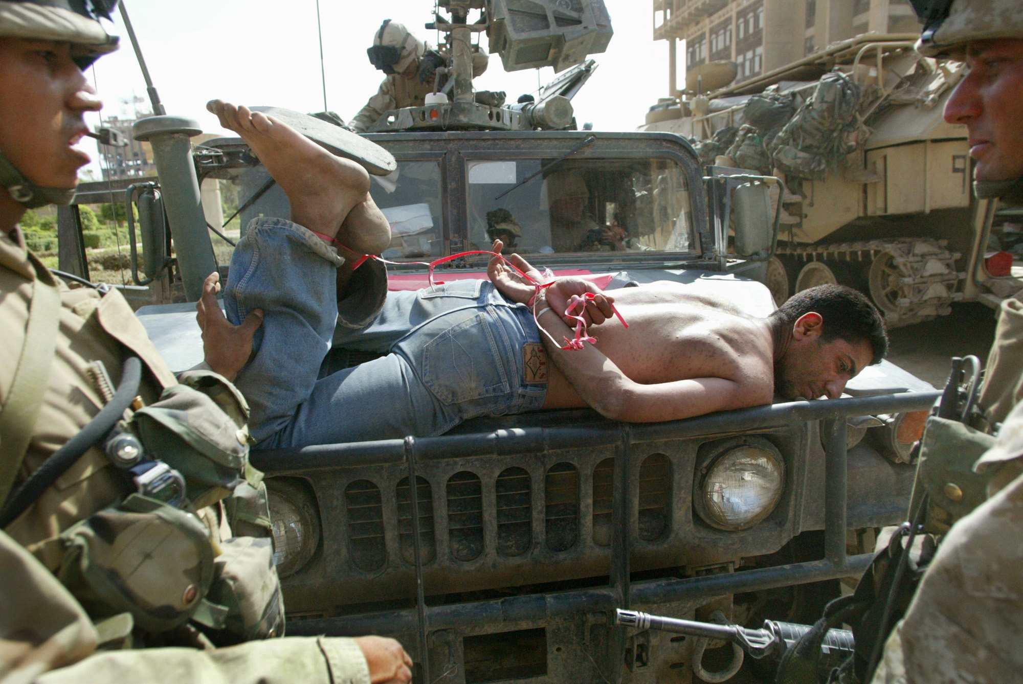 A man accused of looting at a Baghdad bank, is brought to a US military base tied to the hood of a Humvee in Baghdad, Iraq,  April 14, 2003.