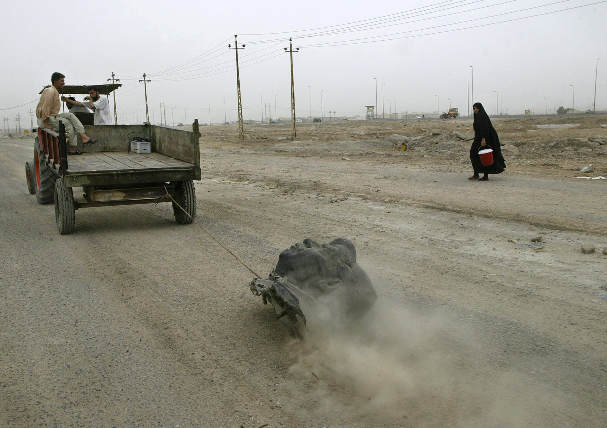 Civilians use a tractor to drag the head of a decapitated Saddam Hussein statue down a gravel road on the edge of Basra, Iraq, April 10, 2003.