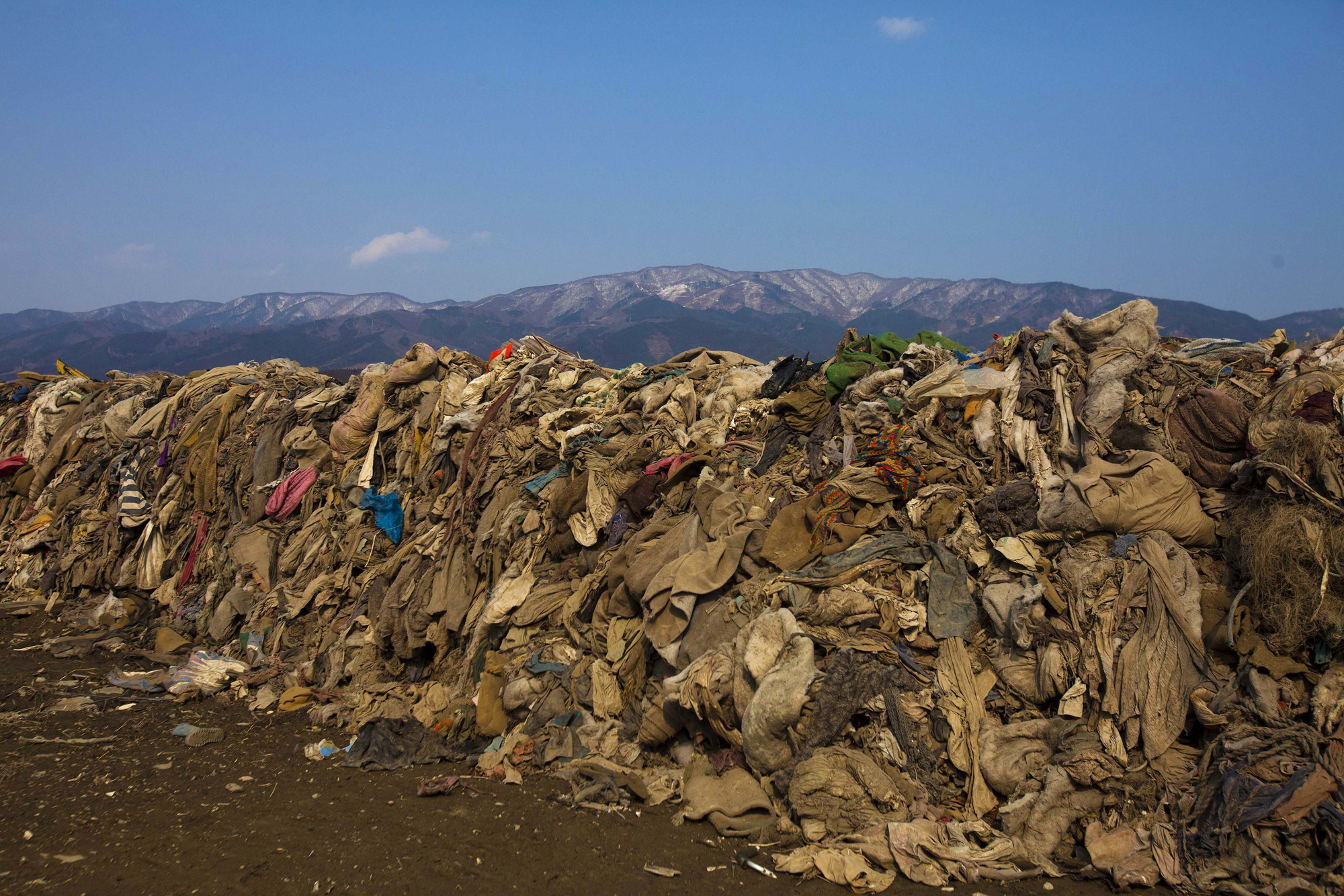 Clothing, lying in heaps at the site of a neighborhood destroyed by the tsunami, is piled up by clearing crew in Rikuzentakata, Iwate Prefecture, northern Japan on Feb. 21, 2012.