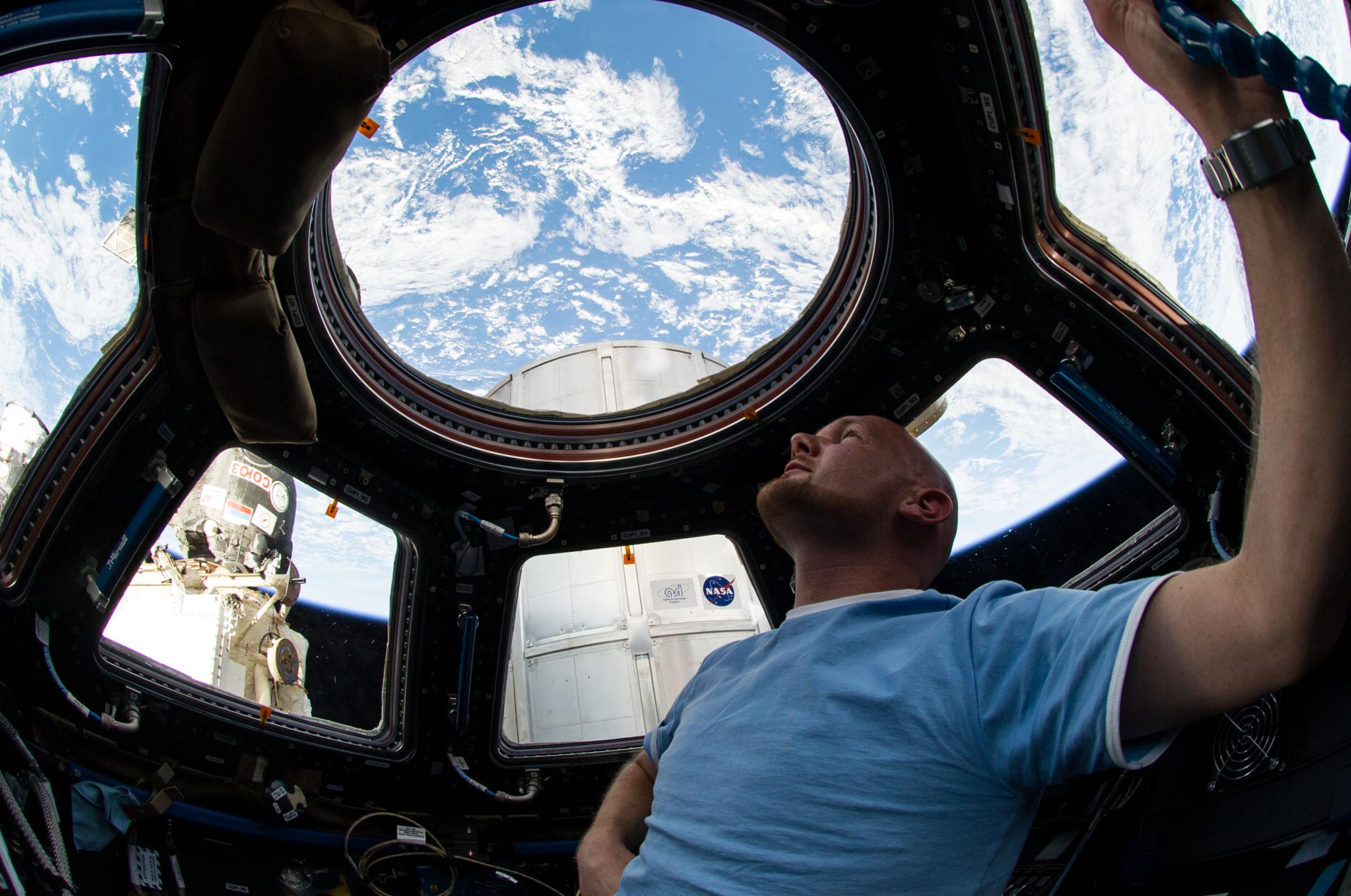 Astronaut Alexander Gerst enjoys the view of Earth from the windows in the Cupola of the International Space Station. A blue and white part of Earth is visible through the windows.