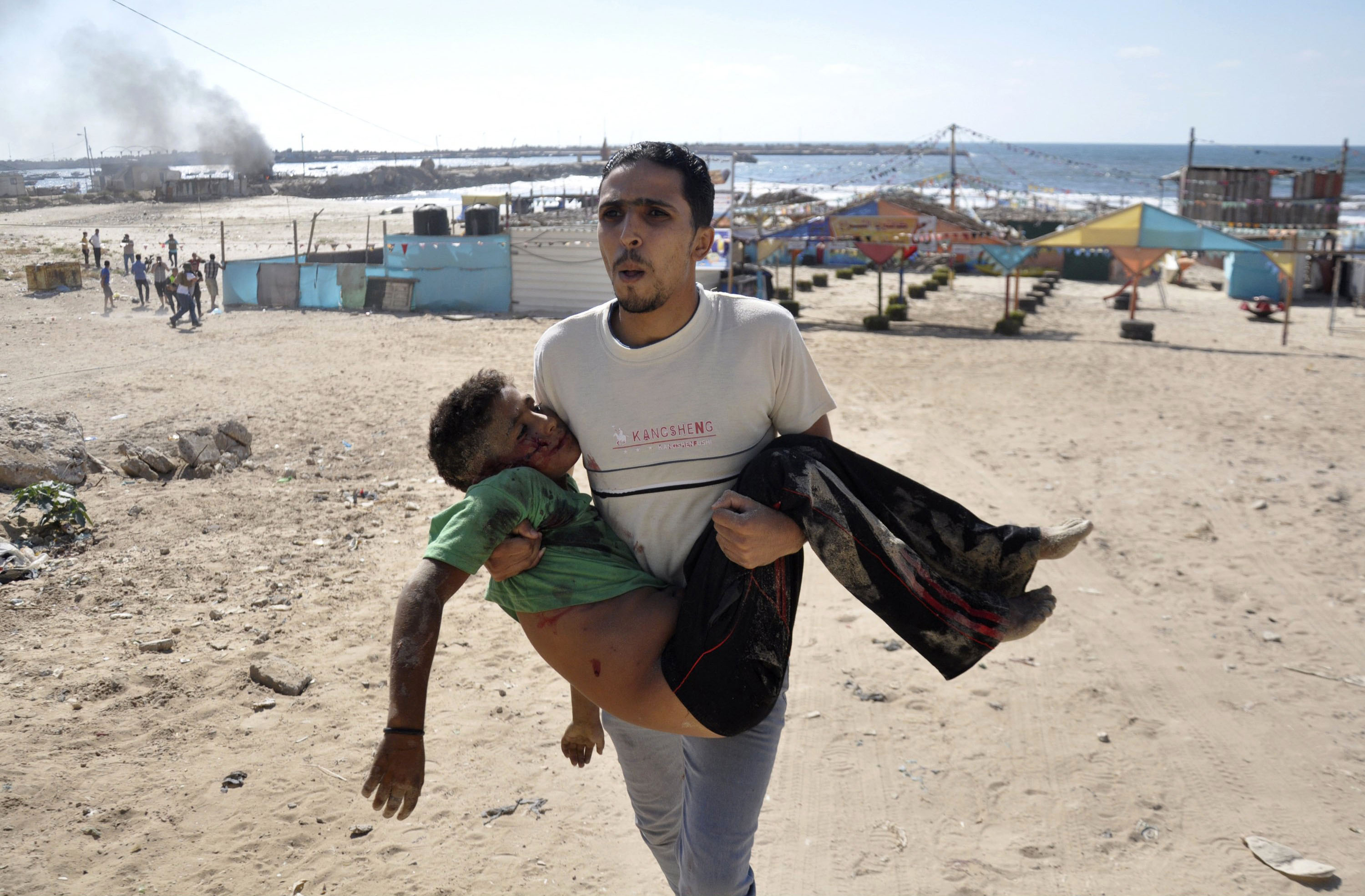 A Palestinian man carries the body of a boy, one of four whom medics say were killed by a shell fired by an Israeli naval gunboat, on a beach in Gaza City. (Mohammed Talatene—Reuters)