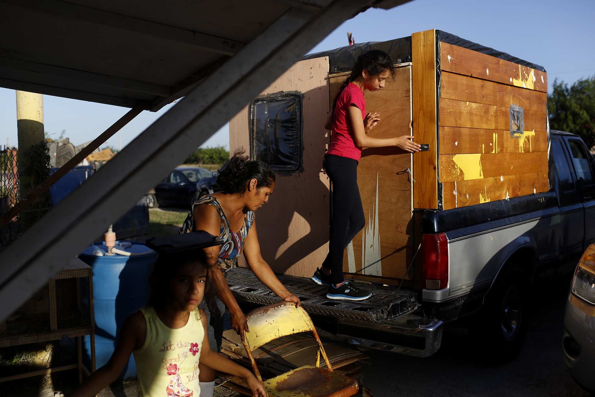 (Left to right) Jazlyn, Cynthia and Briana, who is leaving the sleeping compartment. The sleeping compartment is made from found materials and firework boxes. Cynthia, Nelson and Jazlyn sleep here, Hidalgo, Texas, July 1, 2014.