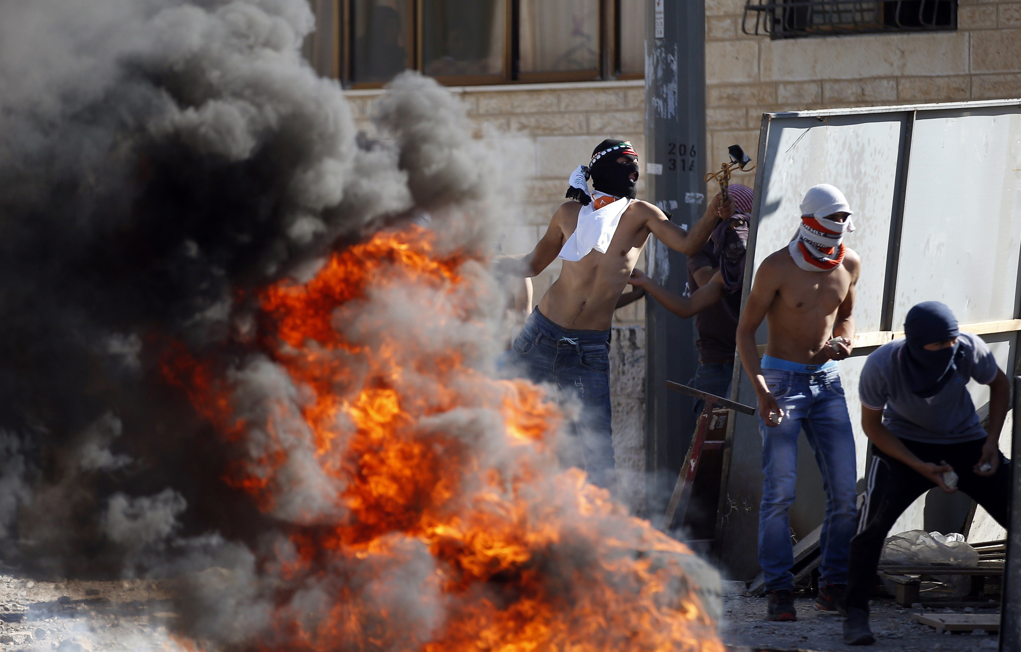 Masked Palestinian protesters throw stones towards Israeli police during clashes in the Shuafat suburb of Jerusalem, on July 2.
