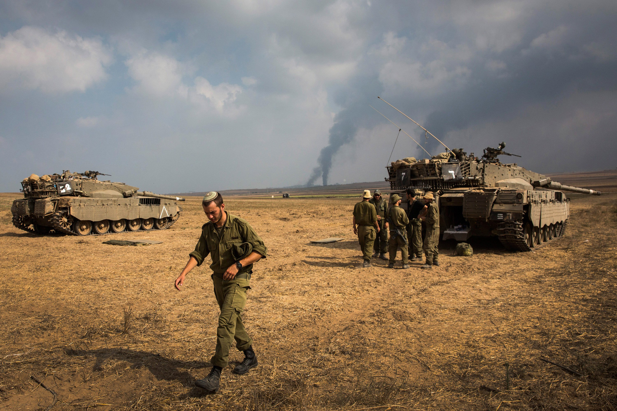 Israeli soldiers stand near their tank while smoke due to airstrikes and shelling rises from Gaza on July 22, 2014 near Sderot, Israel.
