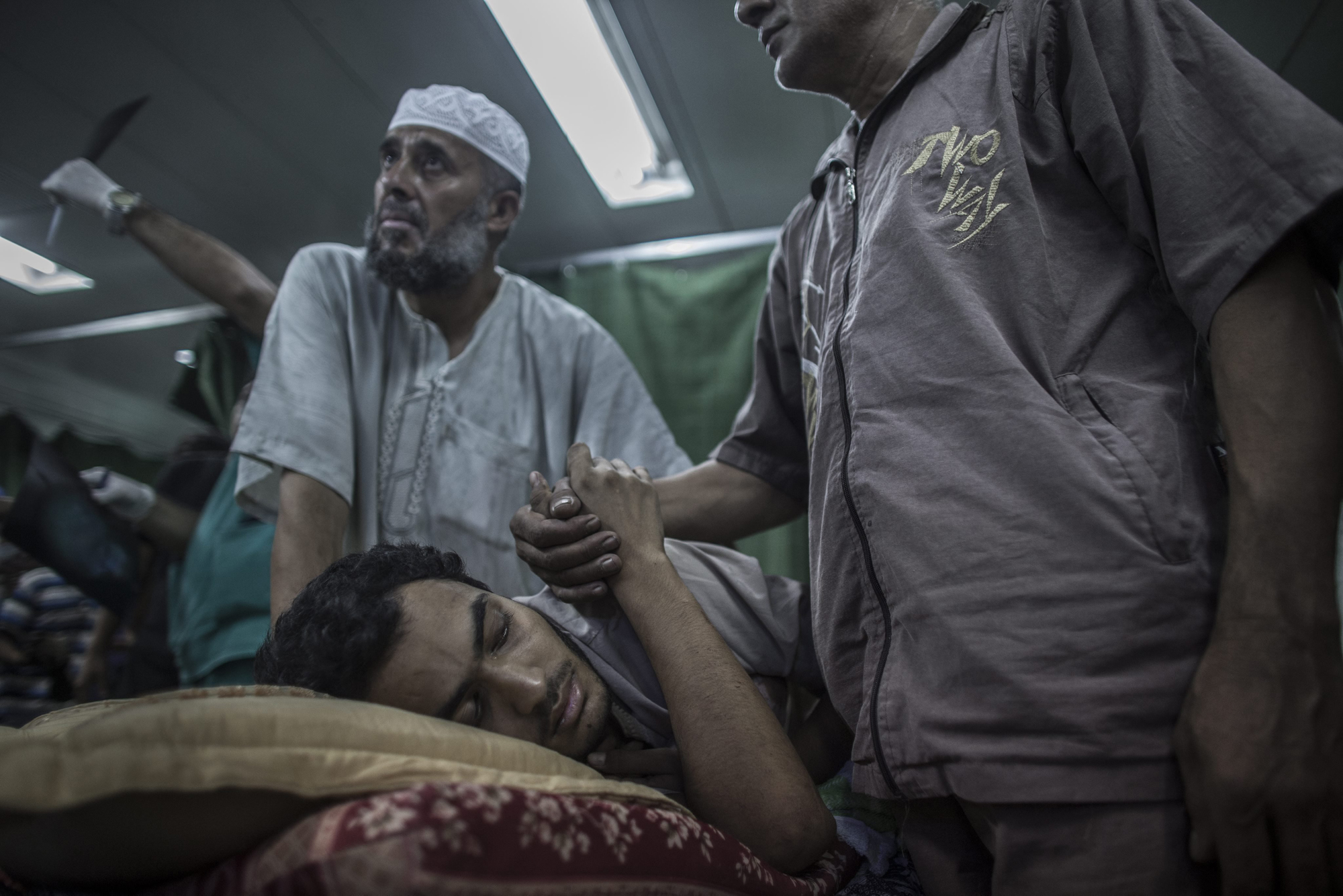 A relative holds the hand of a Palestinian man, who was injured when a UN school used as a shelter for internally displace people came under Israeli shelling, at the emergency room of the Kamal Adwan hospital in Beit Lahia, northern Gaza Strip, July 30, 2014.