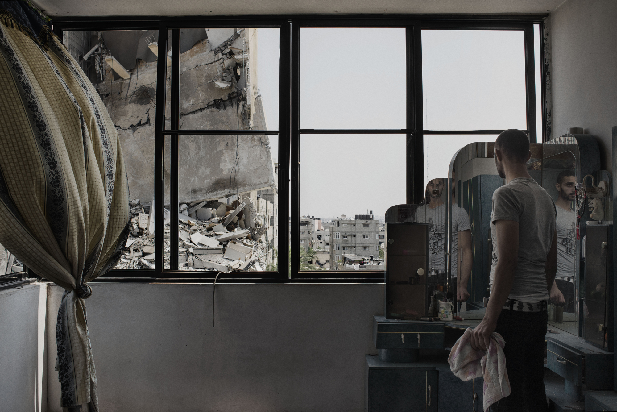 A Palestinian man looks through the window of his house to buildings damaged by an overnight airstrike in Gaza City, July 22, 2014.