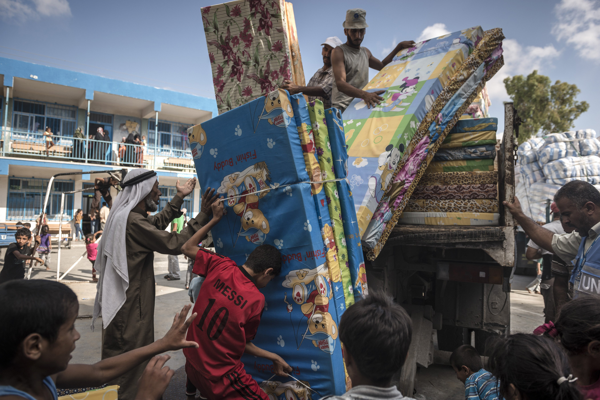Palestinian refugees unload mattresses at a United Nations shelter in Rafah, Gaza Strip, July 19, 2014.