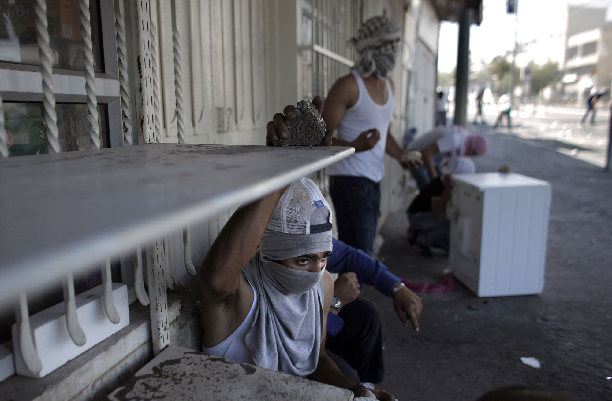 Masked Palestinian protestors take cover as they throw stones toward Israeli police during clashes in Shuafat suburb of Jerusalem, on July 2.