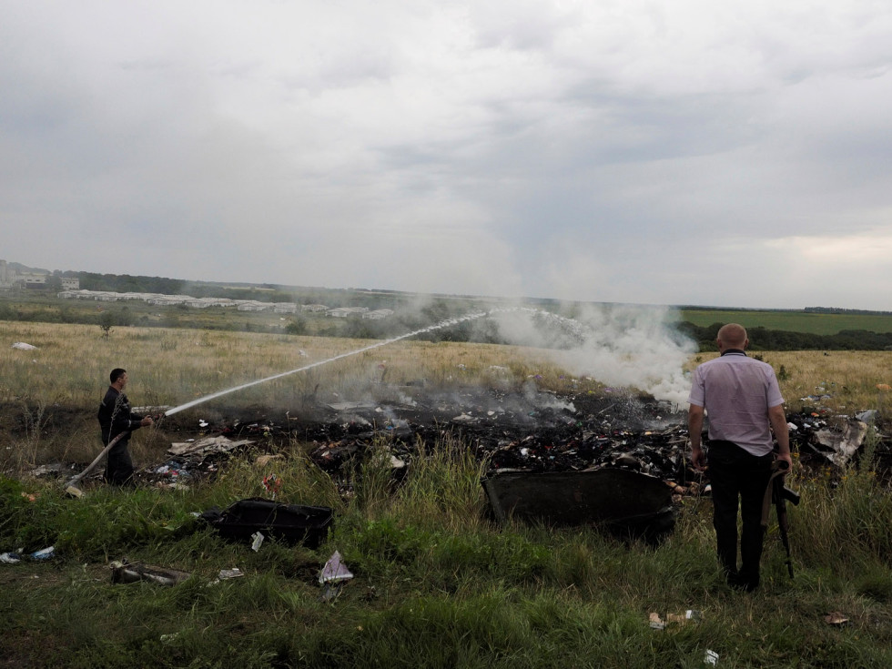 A firefighter and an armed man look at the remains and the corpses of passengers aboard Malaysia Airlines flight MH17 that was shot down over eastern Ukraine, July 17, 2014.