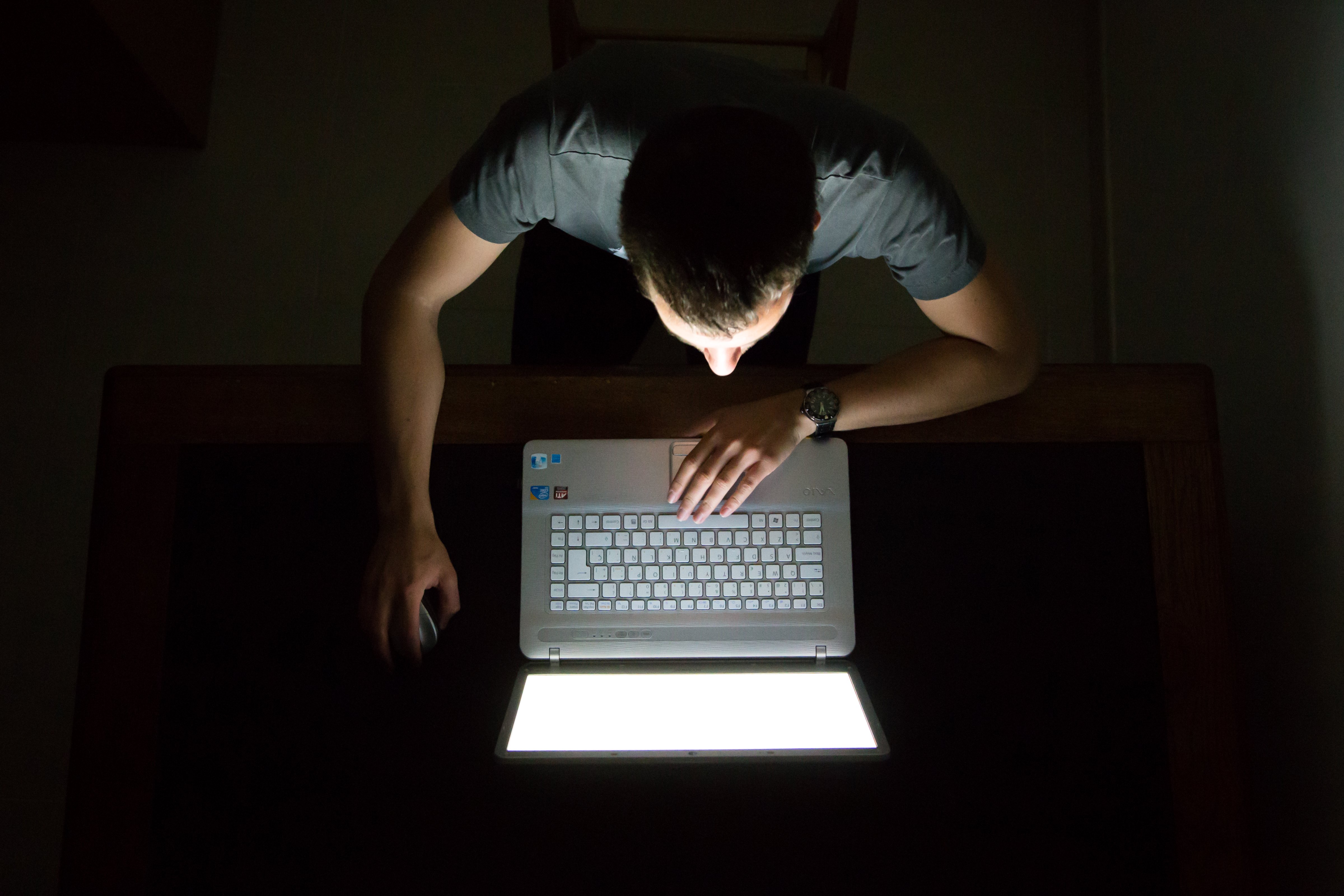 Guy checking internet with laptop at late night with dark room, view from above. (Getty Images)