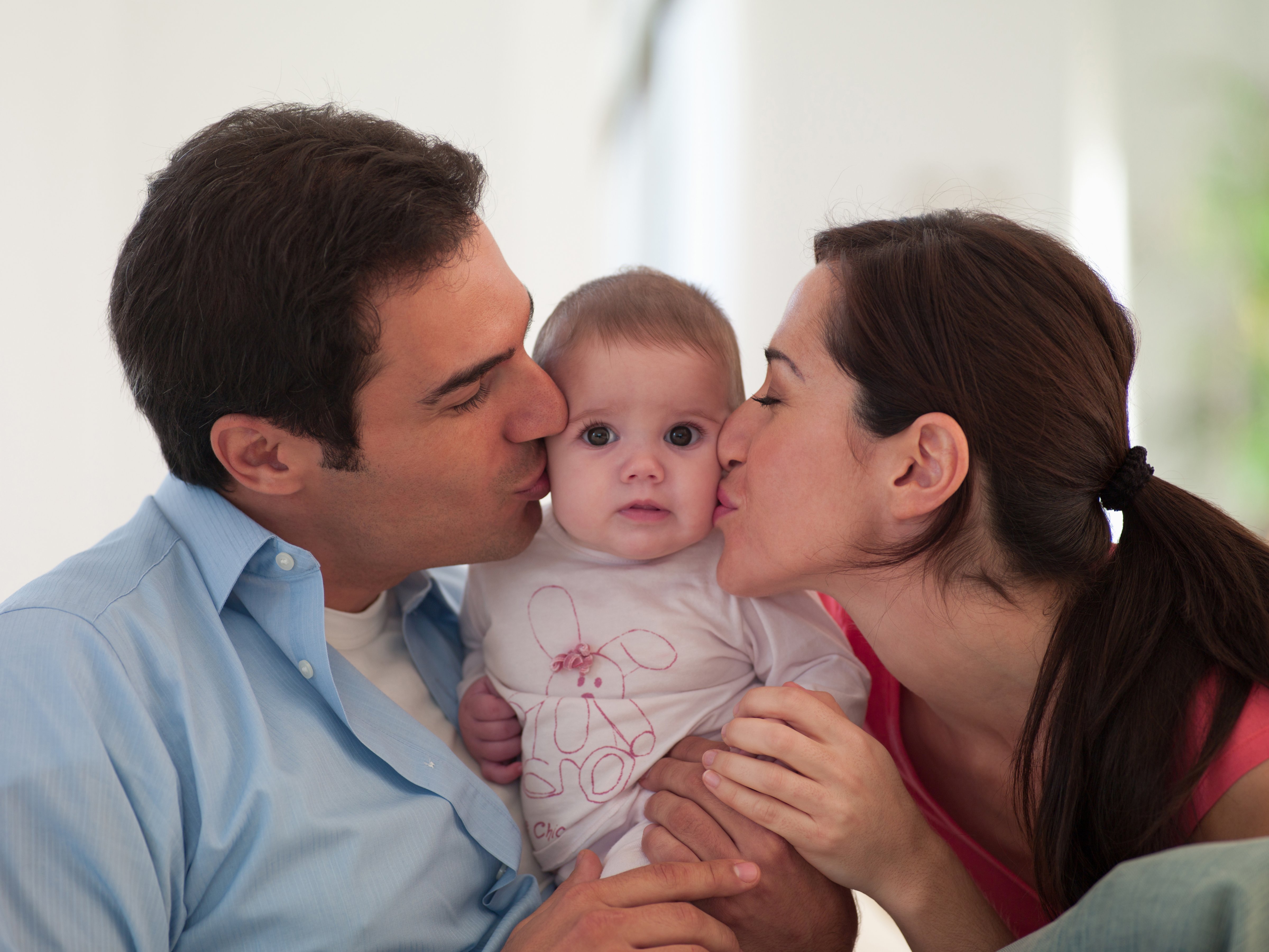 Mother and father are shown kissing their baby daughter. (Chris Ryan—OJO Images RF/Getty Images)