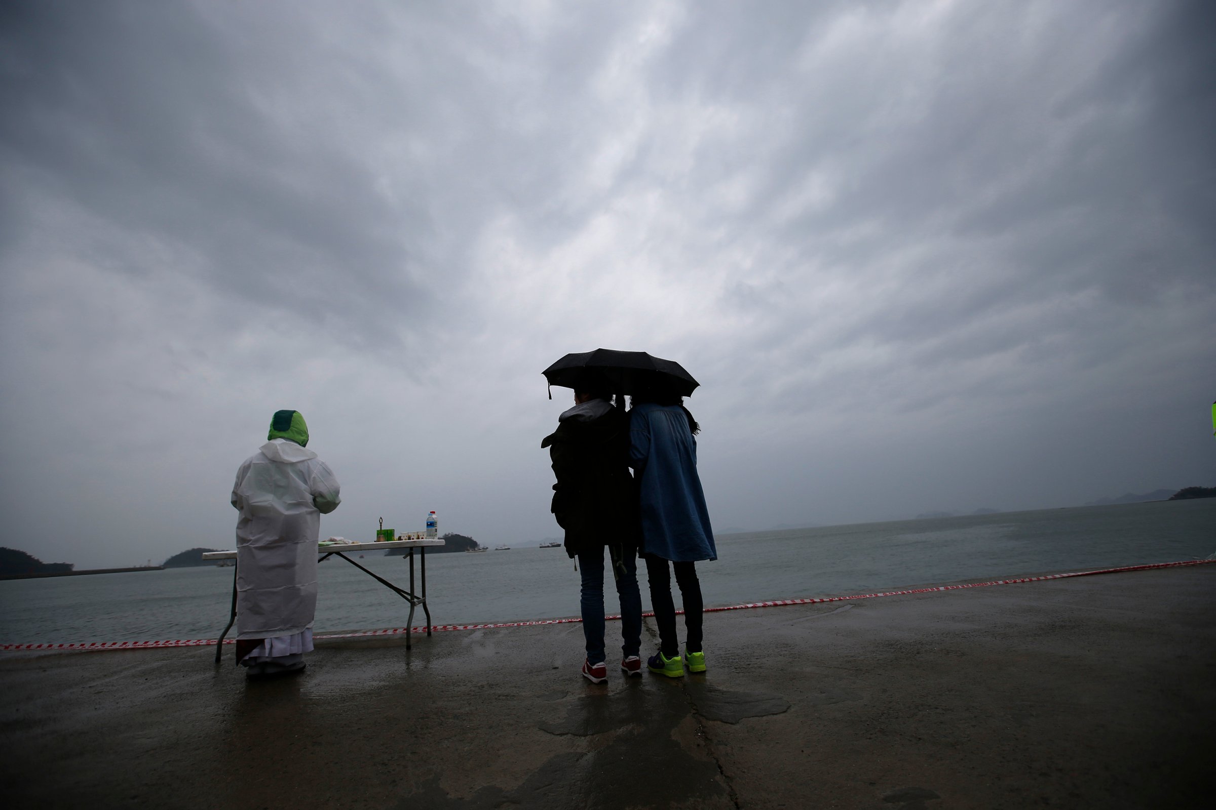 Relatives of a missing passenger onboard the capsized Sewol ferry, looks at the sea while a Buddhist monk prays for the victims at a port in the rain in Jindo