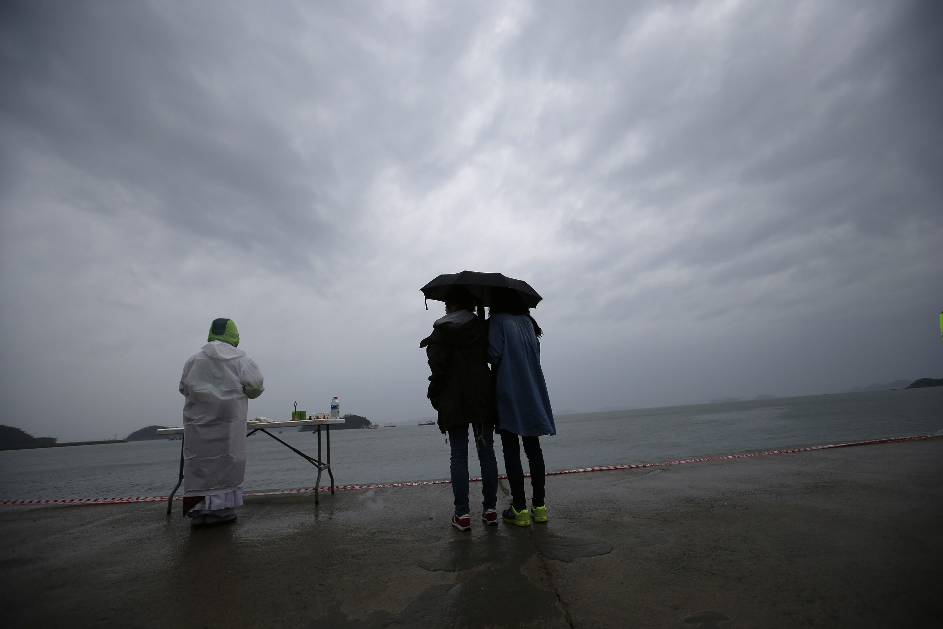 Relatives of a missing passenger onboard the capsized Sewol ferry look at the sea while a Buddhist monk prays for the victims at a port in the rain, where family members wait for news from the search and rescue team on April 27, 2014. (Kim Kyung Hoon—Reuters)