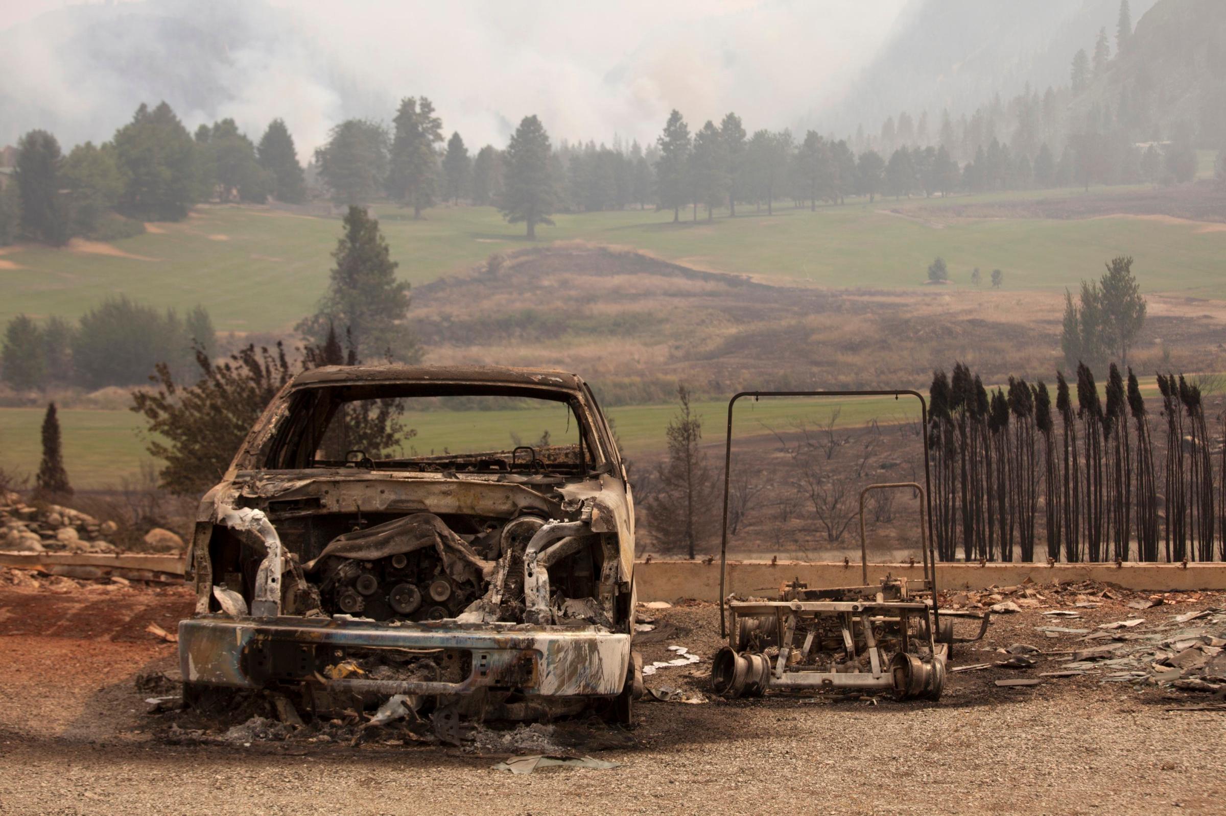 A damaged vehicle is pictured near Alta Lake Golf Course after it was consumed by the Carlton Complex Fire, which can be seen burning in the distance, near Pateros