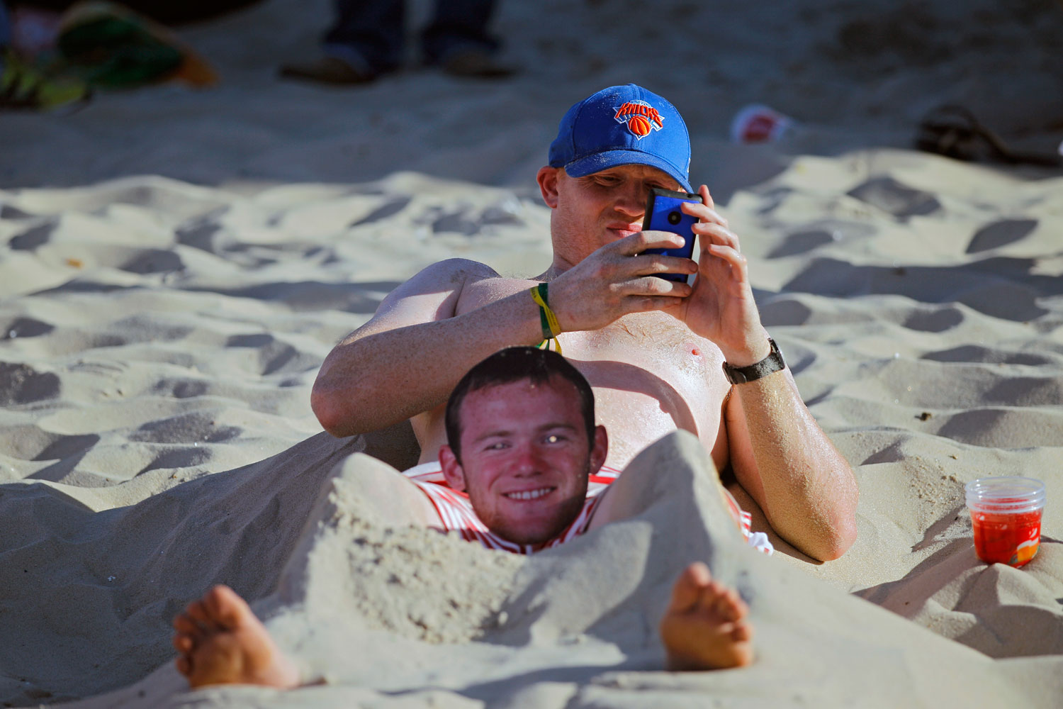 An England fan lies on the sand of Copacabana beach with a mask of English soccer star Wayne Rooney between his legs, in Rio de Janeiro on June 14, 2014.