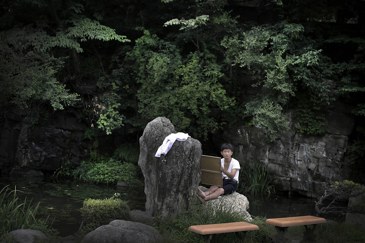 A boy sits on a rock as he sketches at the Moranbong (Moran Hill) in Pyongyang, Jul. 31, 2014. With the heat and humidity of summer setting in, one of the most popular locations is Moranbong, a short walk from Kim Il Sung Square, which is known for its shady walking paths, vistas of the city and grassy fields.