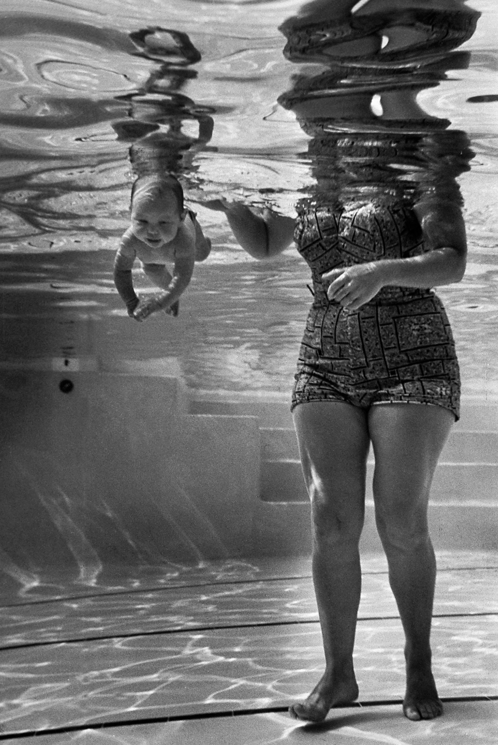 The "world's youngest swimmer," 9-week-old Julie Sheldon, cruises underwater next to her grandmother, Mrs. Jen Loven, a children's swimming instructor in 1954 Los Angeles.