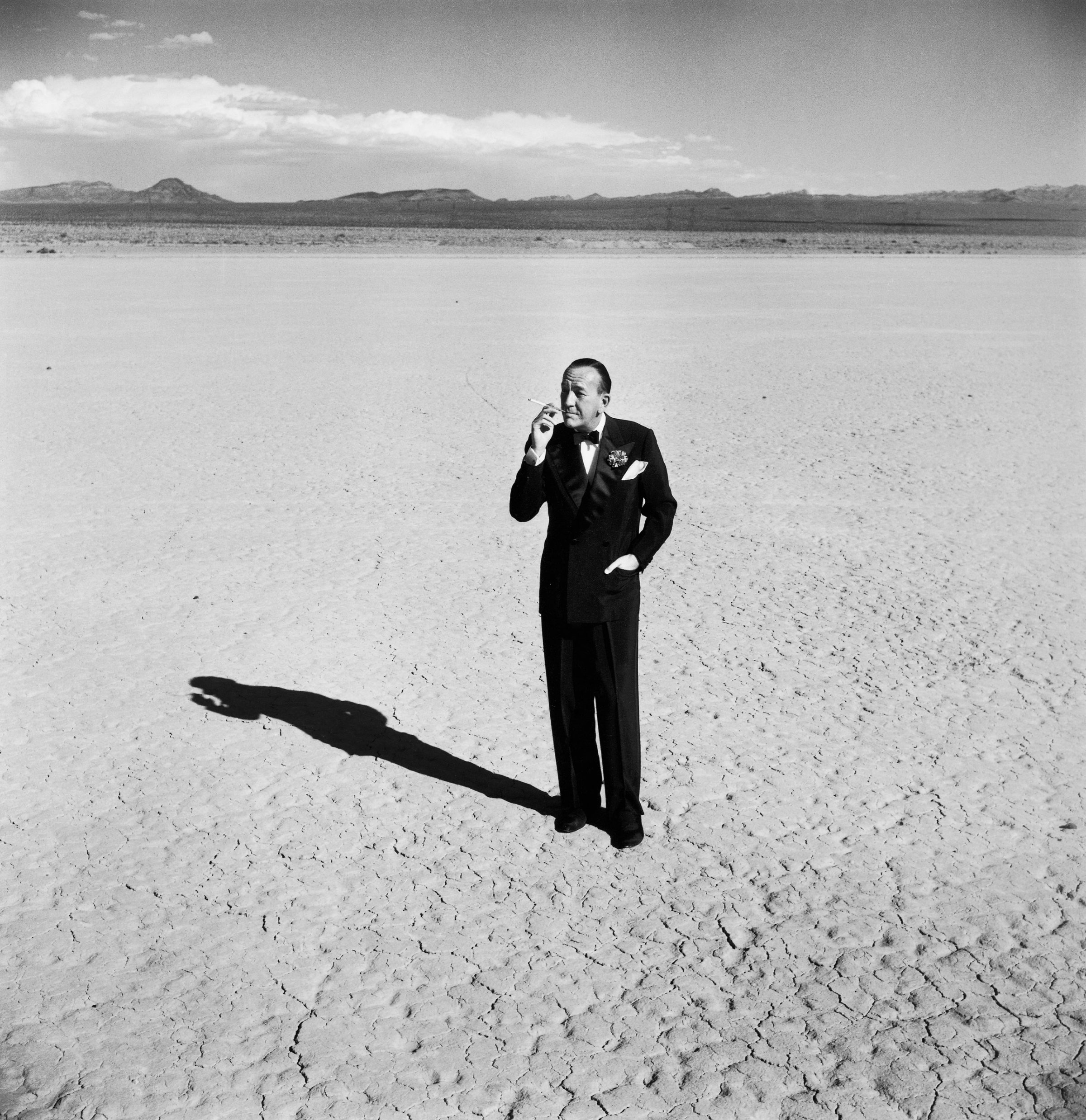 Noël Coward standing in a dry lake bed, Nevada, 1955.