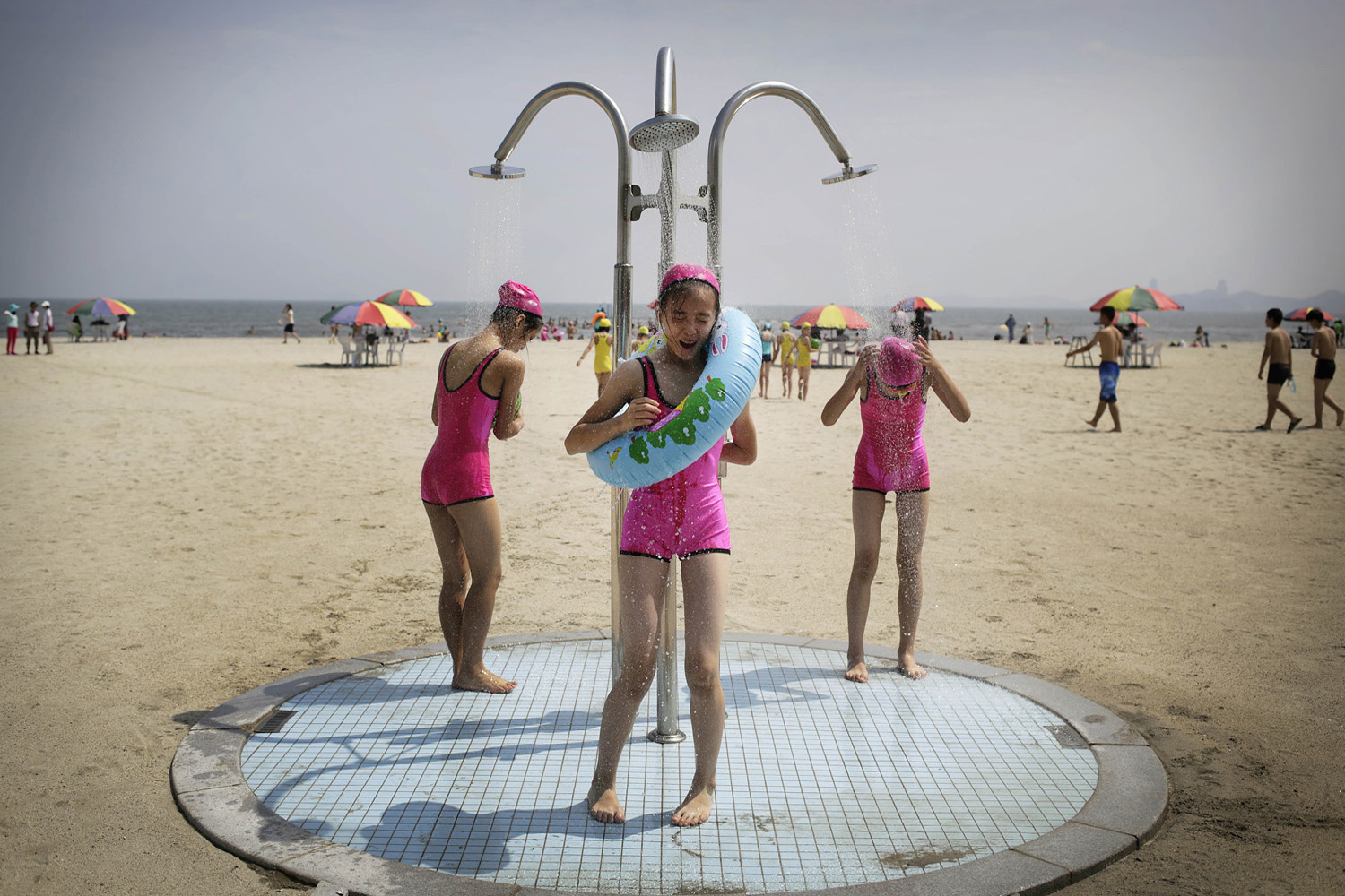 Girls in similar bathing suits stand under a shower at the Songdowon International Children's Camp in Wonsan, Jul. 29, 2014.