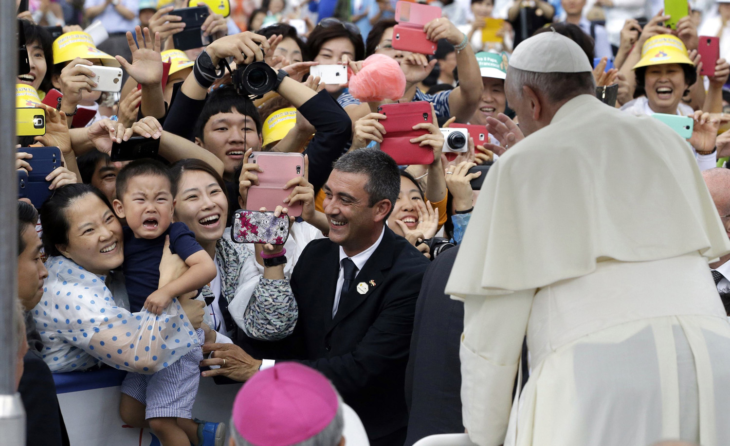 Pope Francis blesses a crying child who does not want to be separated from his mother to be blessed by the pope, as a Vatican gendarmerie (C) smiles, at the pope's arrival for a closing Holy Mass of the 6th Asian Youth Day at Haemi Castle in Haemi, Seoul on Aug. 17, 2014.