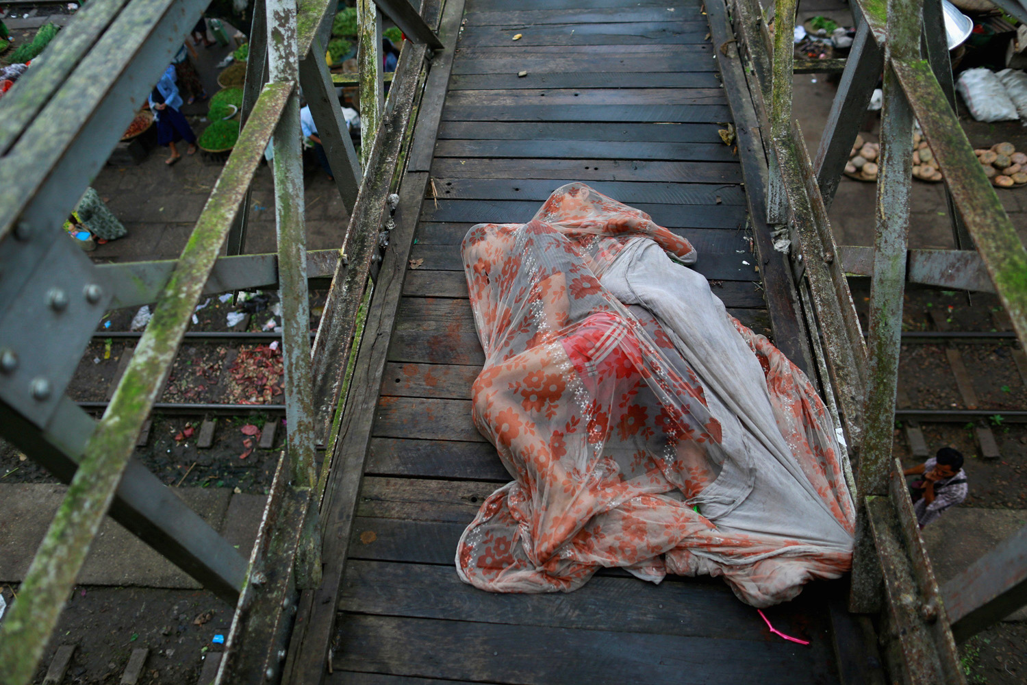 Men sleep covered with a mosquito net on a bridge above a train station outside Yangon